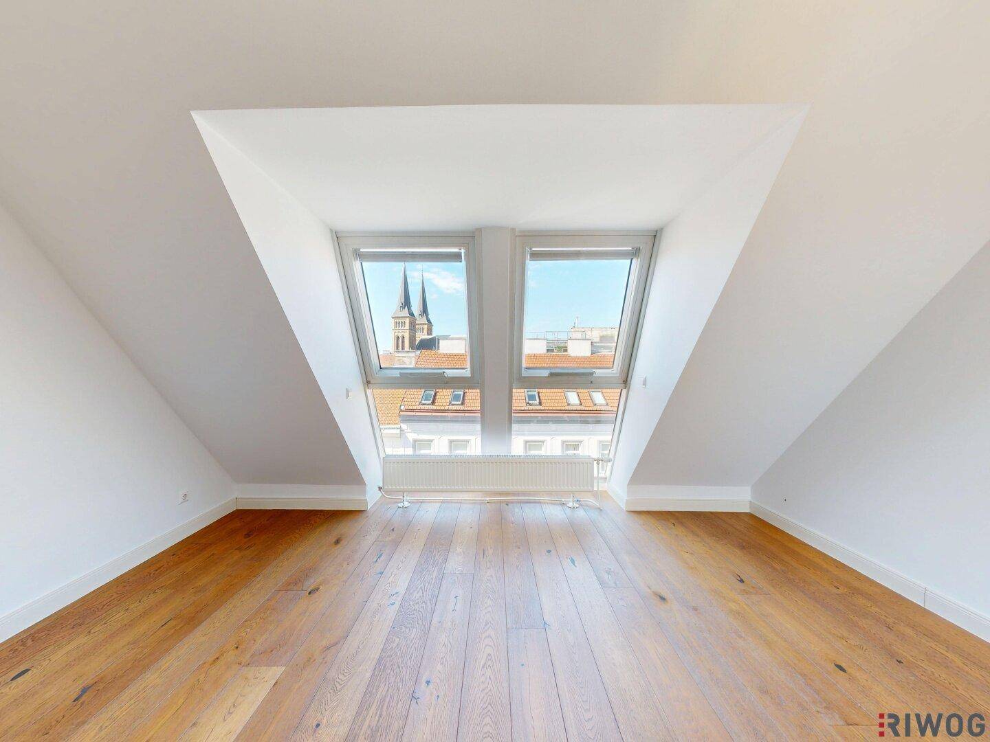 Helles Zimmer mit Holzboden, Dachschrägen und Blick auf die Kirchtürme der Stadt.