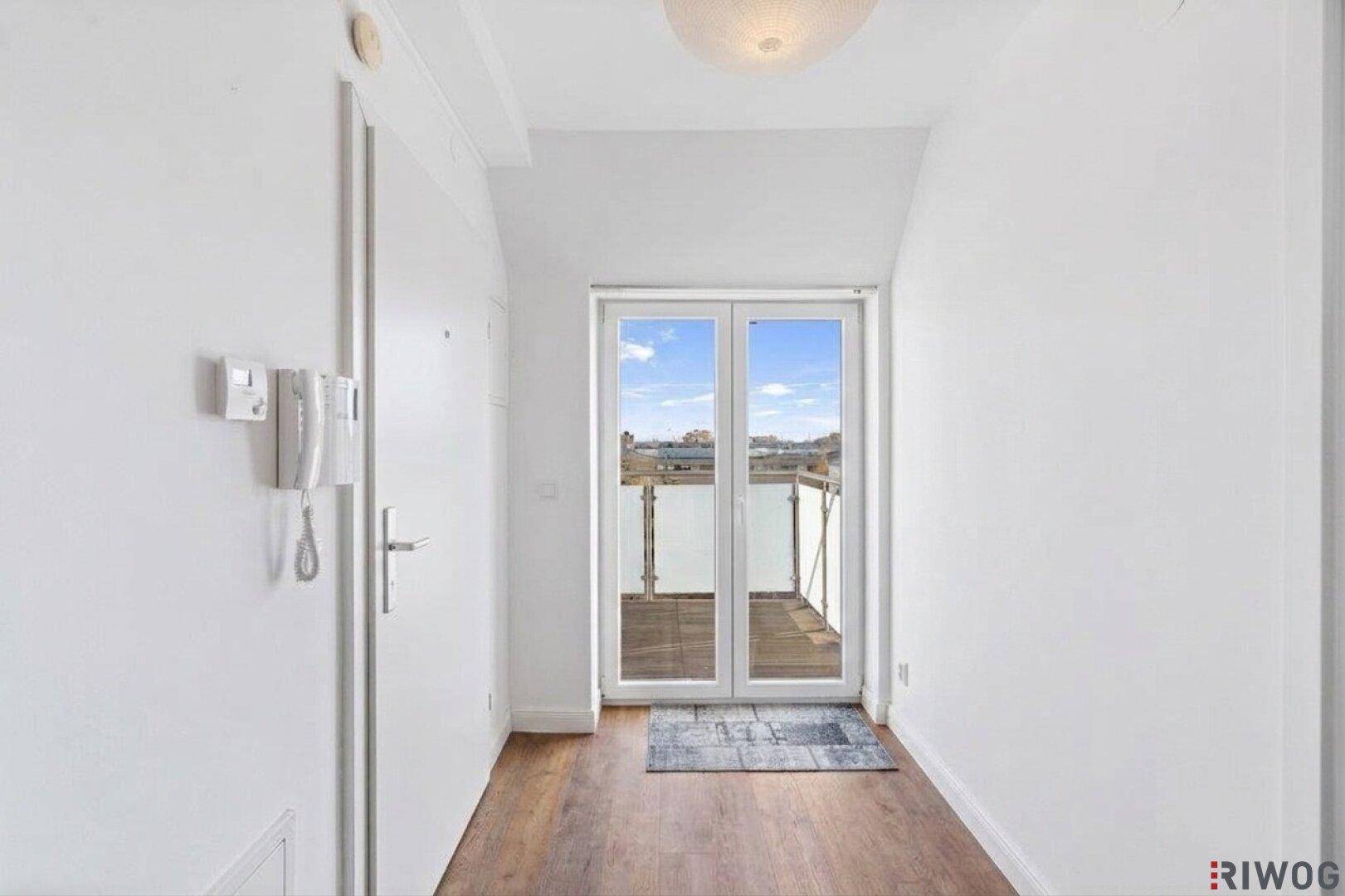 Heller Flur mit Holzboden und direktem Zugang zu einem sonnigen Balkon.