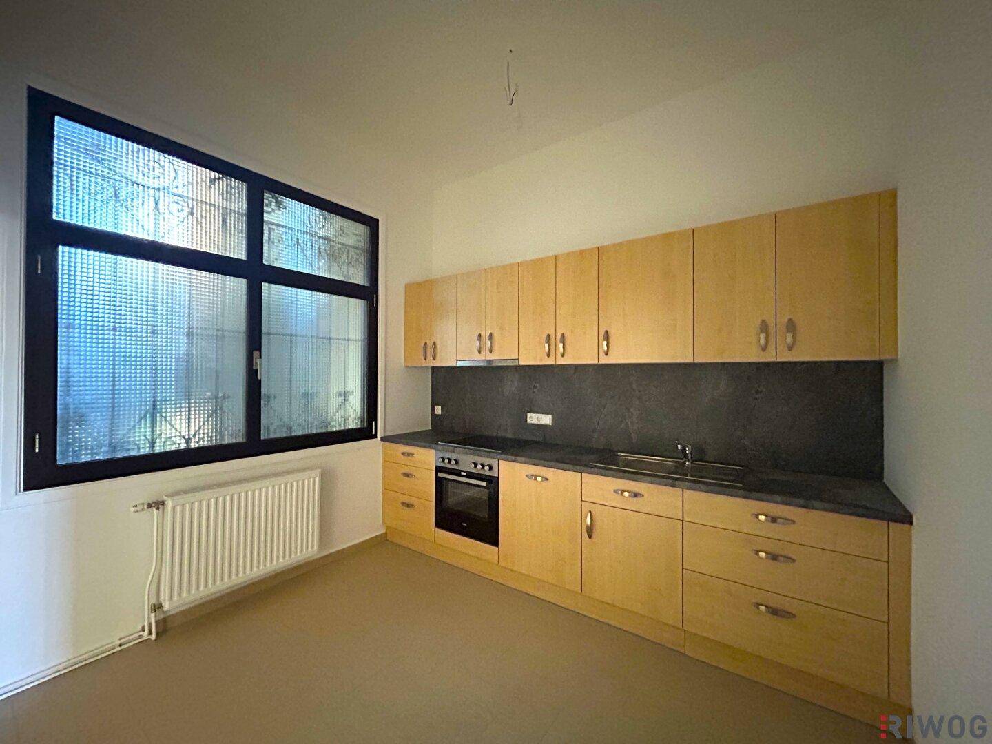 Funktionale Küche mit hellen Holzschränken, dunkler Arbeitsplatte und integriertem Backofen, gut beleuchtet.