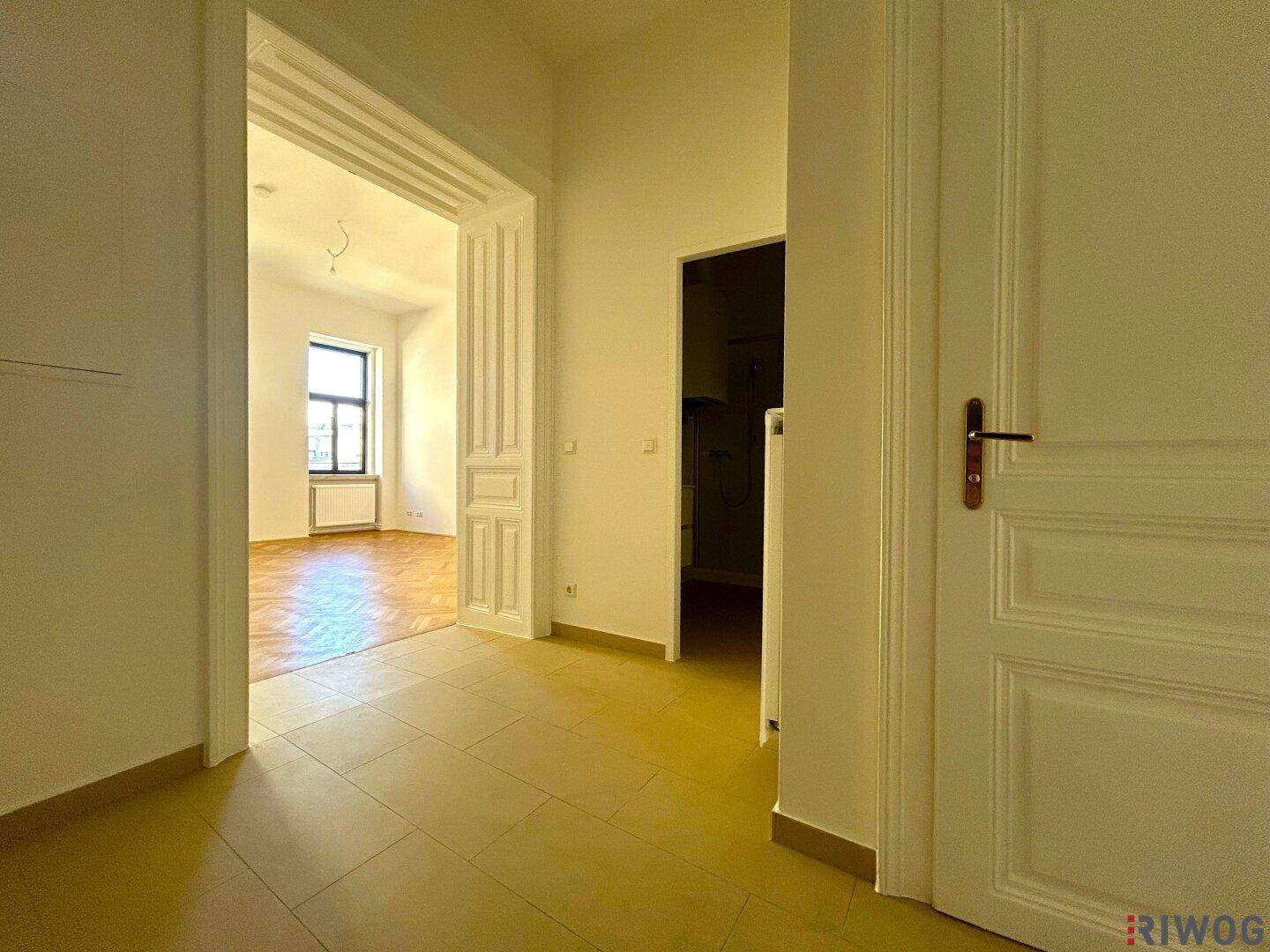 Geräumiger Flur mit Fliesenboden und offenem Durchgang zu einem Zimmer mit Fischgrätparkett.