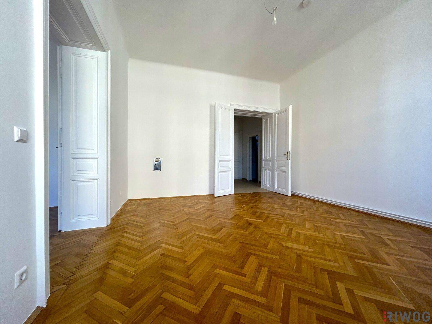 Geräumiges Zimmer mit klassischem Fischgrätparkett und eleganten Doppeltüren zu angrenzenden Räumen.