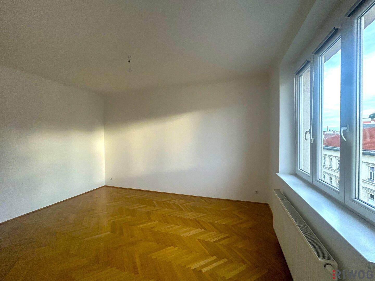Geräumiges Wohnzimmer mit Parkettboden und großen Fenstern, die viel Licht hereinlassen.