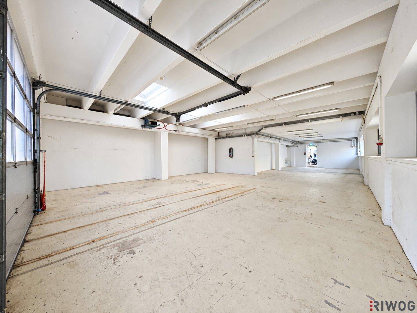Leere, geräumige Lagerhalle mit Betonboden, hohen Decken und einem großen Rolltor, bereit zur Nutzung.