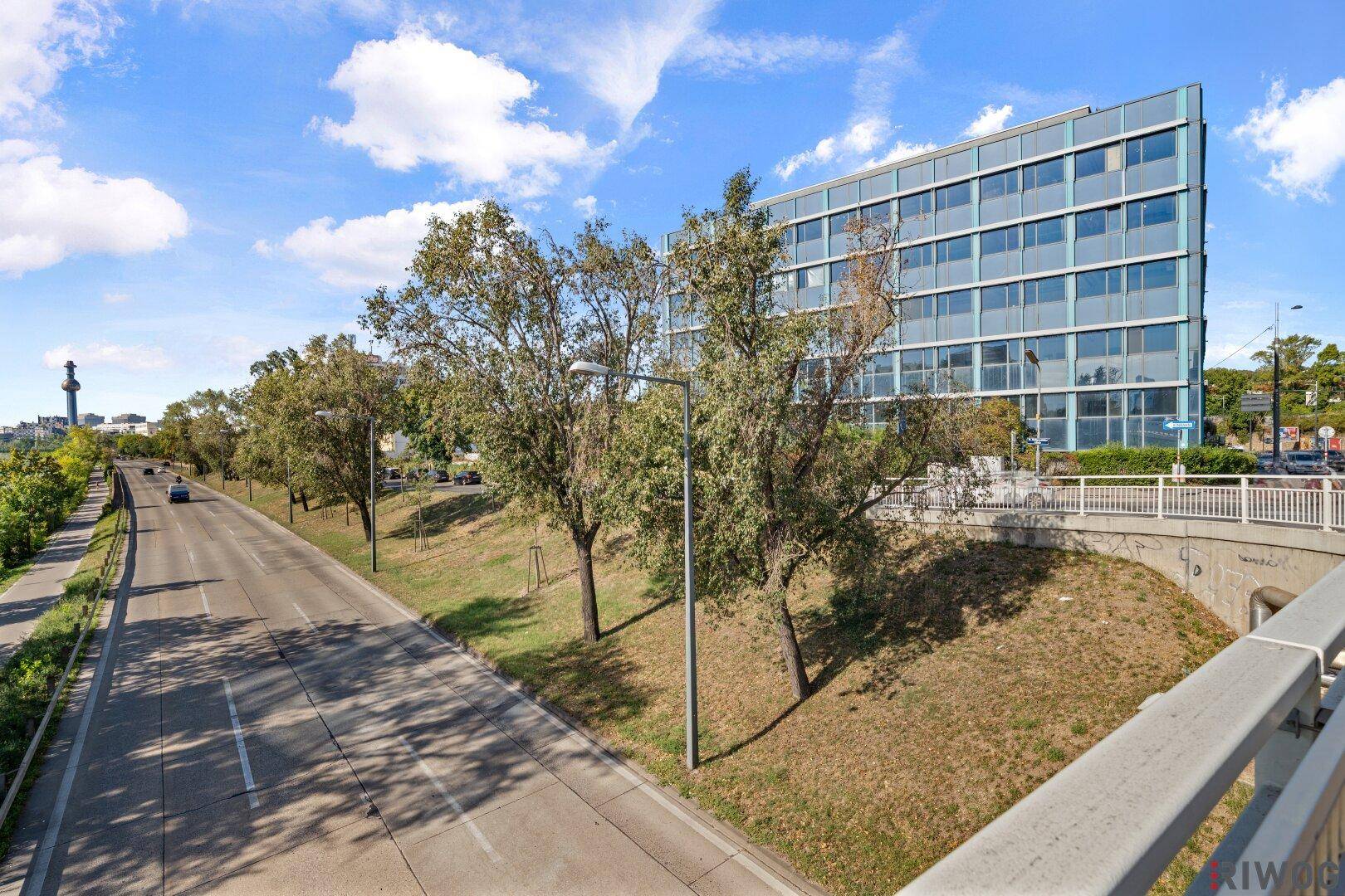 Blick auf das Bürogebäude von einer erhöhten Position mit Straße und Bäumen im Vordergrund.