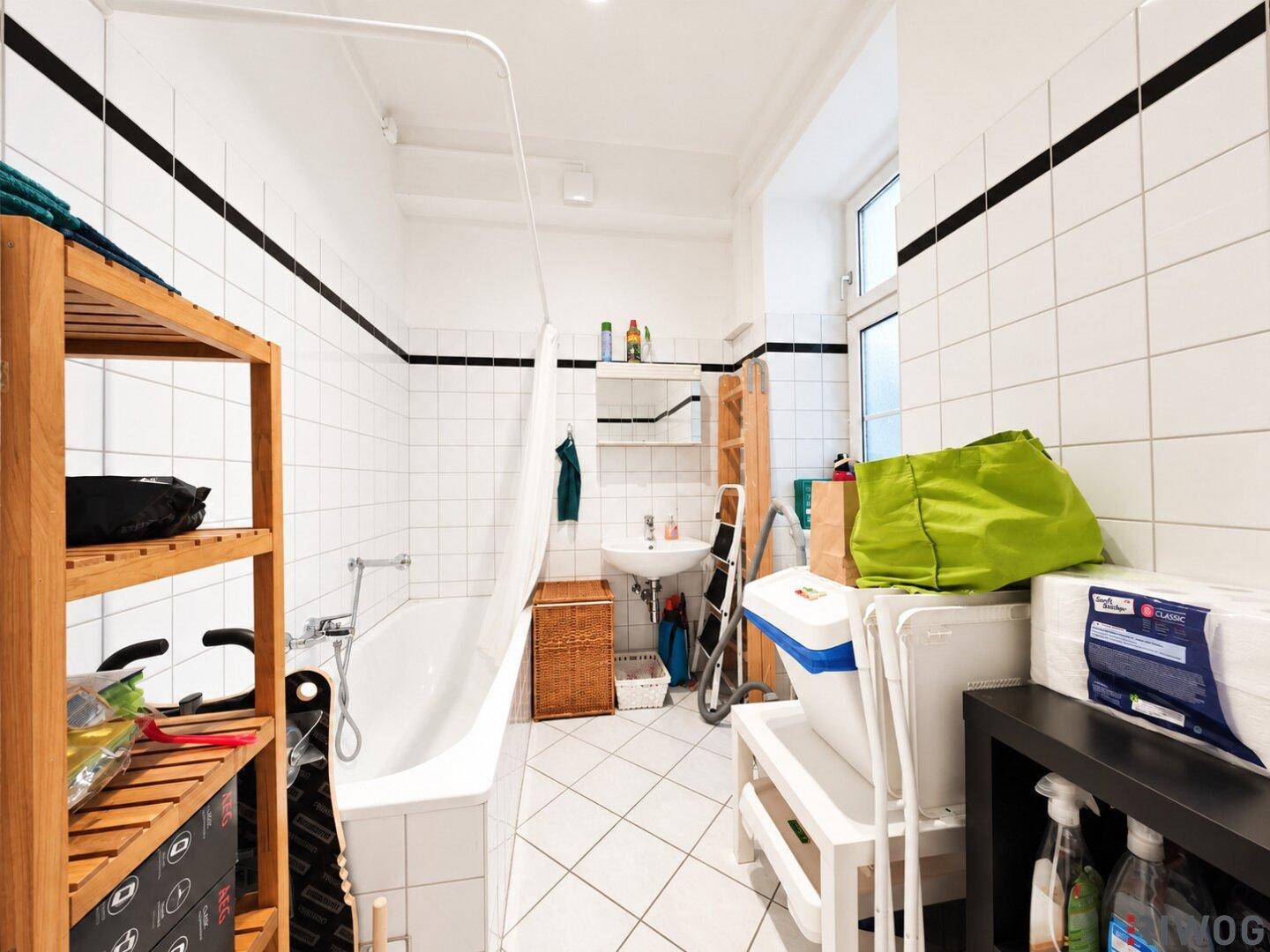 Helles Badezimmer mit Badewanne, weißen Fliesen und einem Fenster.