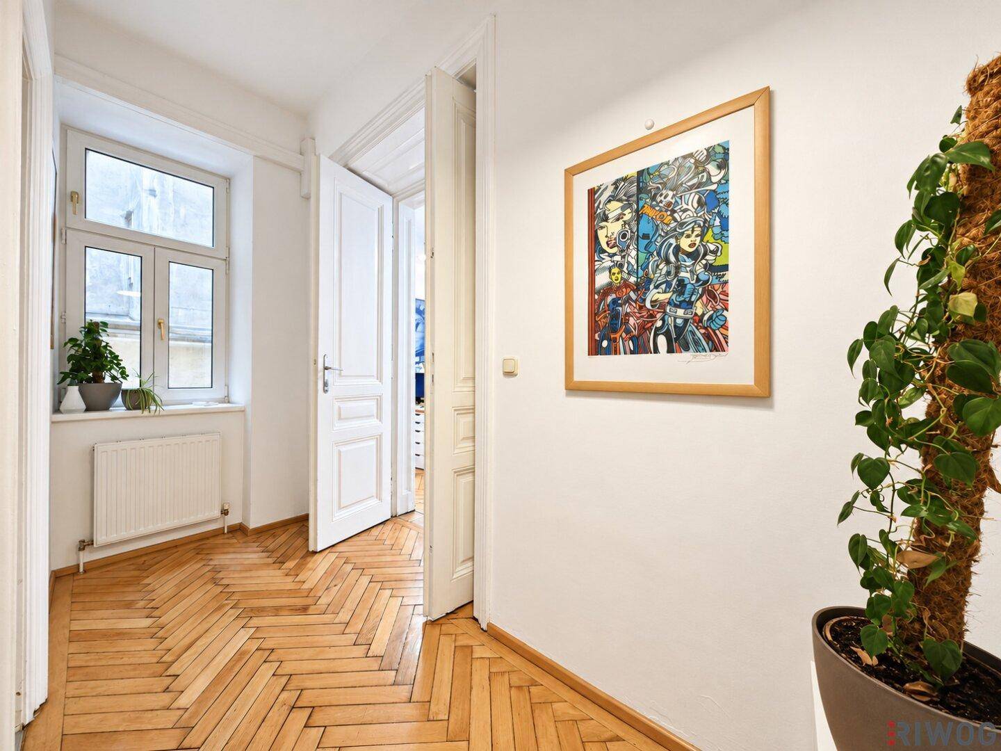 Heller Flur mit Parkettboden, hohen Türen und einem Fenster, das Tageslicht hereinlässt.