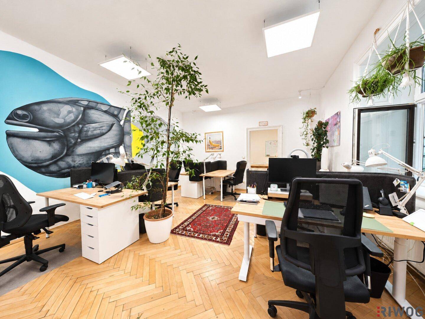 Kreatives Büro mit mehreren Schreibtischen, Parkettboden und einer farbenfrohen Wandmalerei.