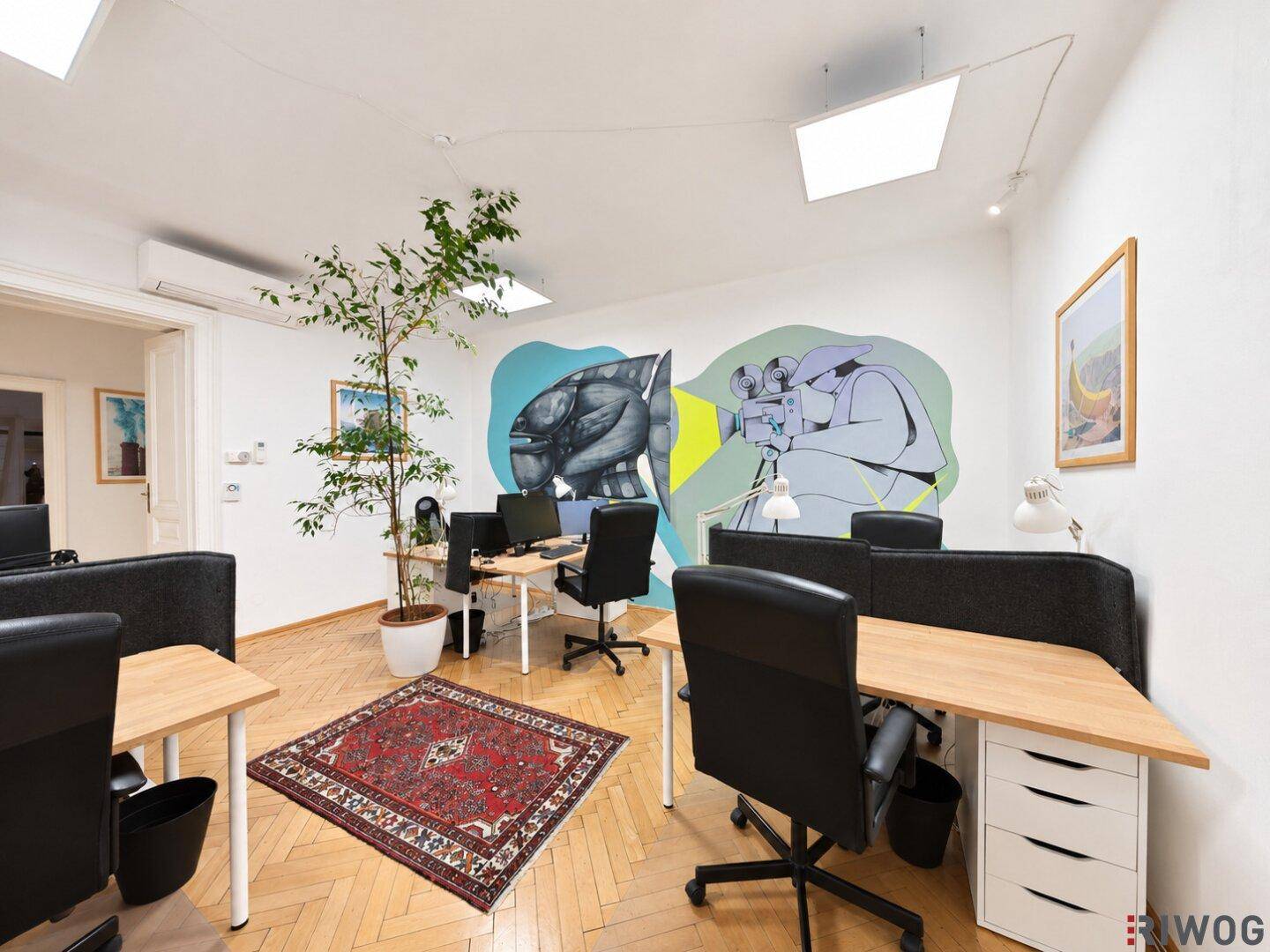 Heller Büroraum mit mehreren Arbeitsplätzen, Parkettboden und kreativer Wandkunst.