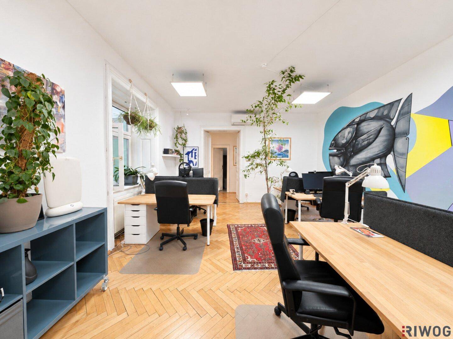 Modernes Büro mit Holzschreibtischen, Parkettboden und einer auffälligen Wandgestaltung.