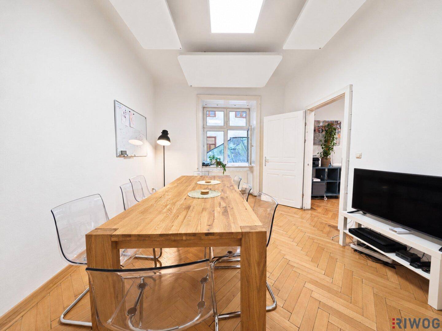 Heller Besprechungsraum mit Holztisch, modernen Stühlen und einem Fenster mit Blick nach draußen.