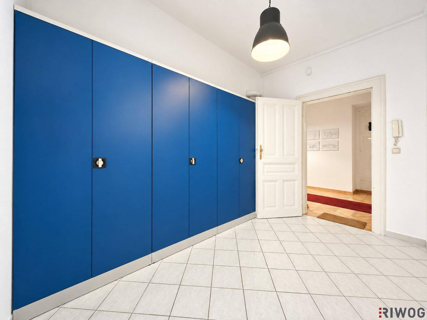 Eingangsbereich mit blauen Schränken, Fliesenboden und einer offenen Tür zu einem weiteren Raum.