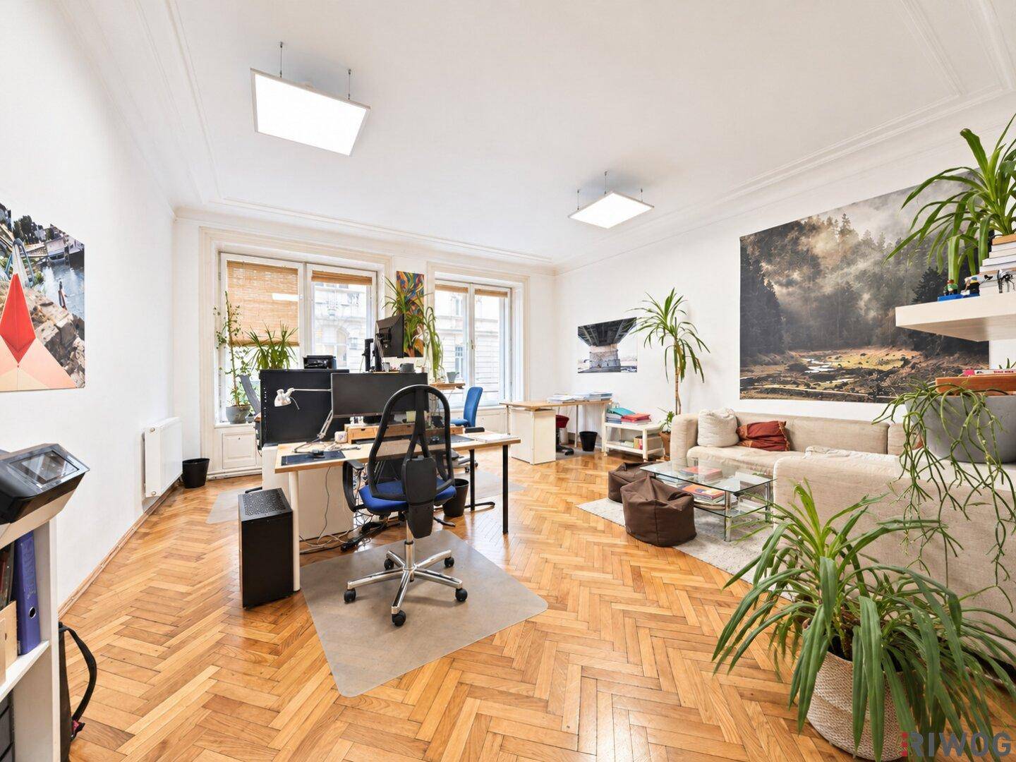 Helles Büro mit Parkettboden, mehreren Arbeitsbereichen und einer gemütlichen Sitzecke mit Sofa.