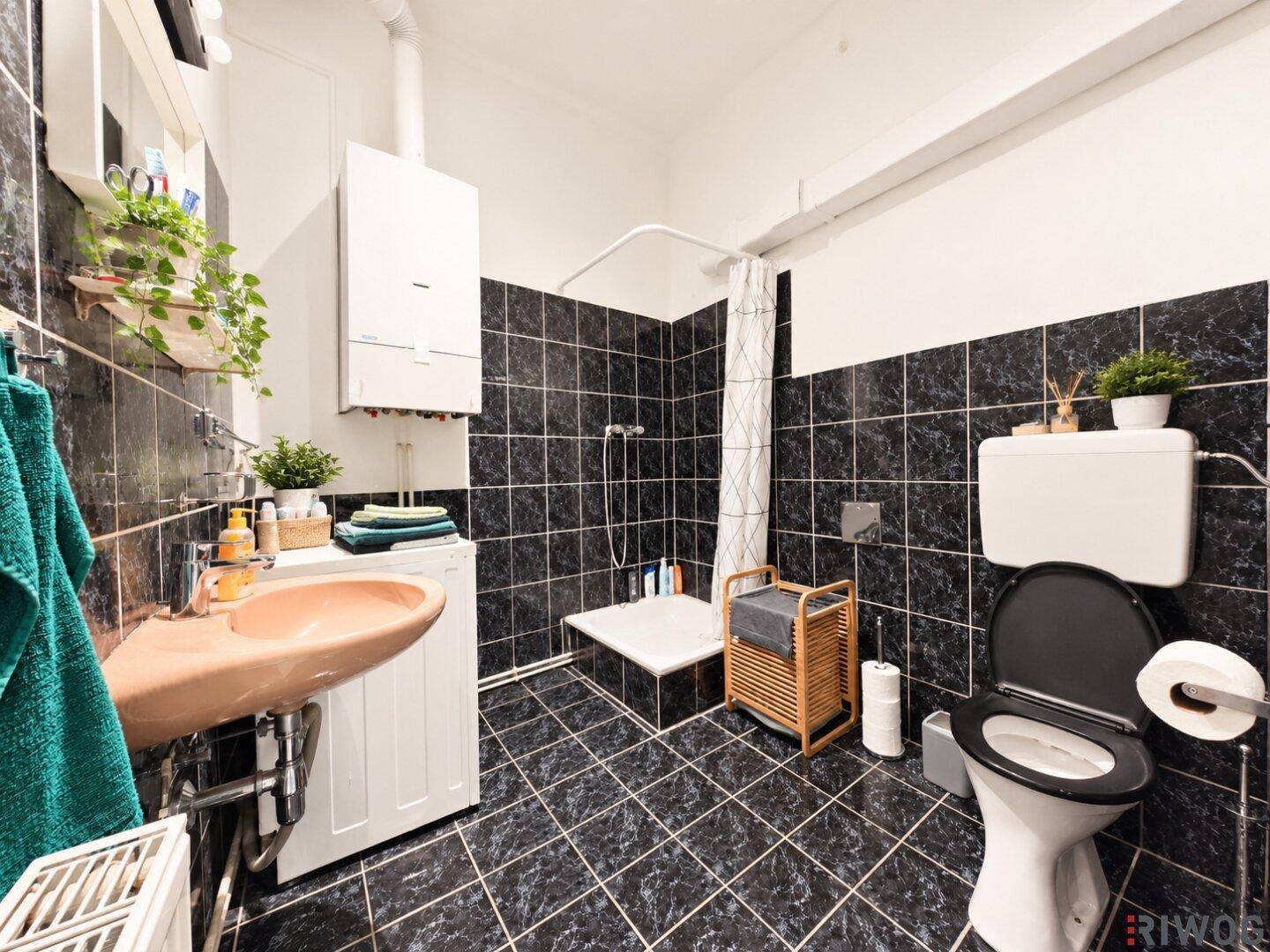Badezimmer mit dunklen Fliesen, Dusche und Waschmaschine.
