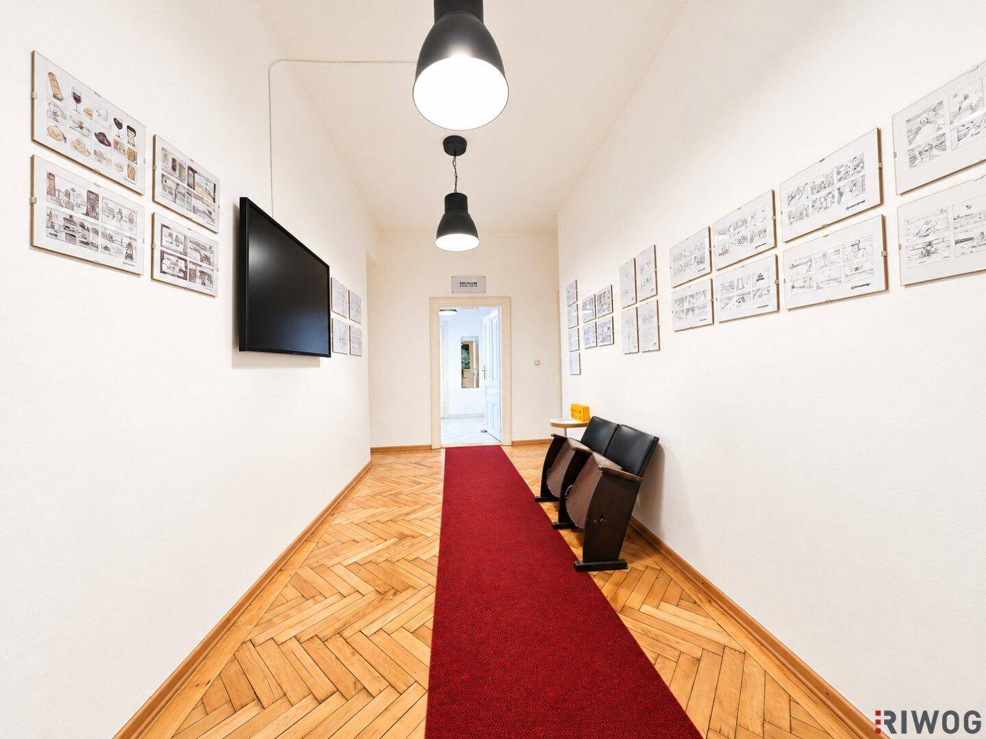 Langer Flur mit Parkettboden, rotem Teppichläufer und Kunstwerken an den Wänden.
