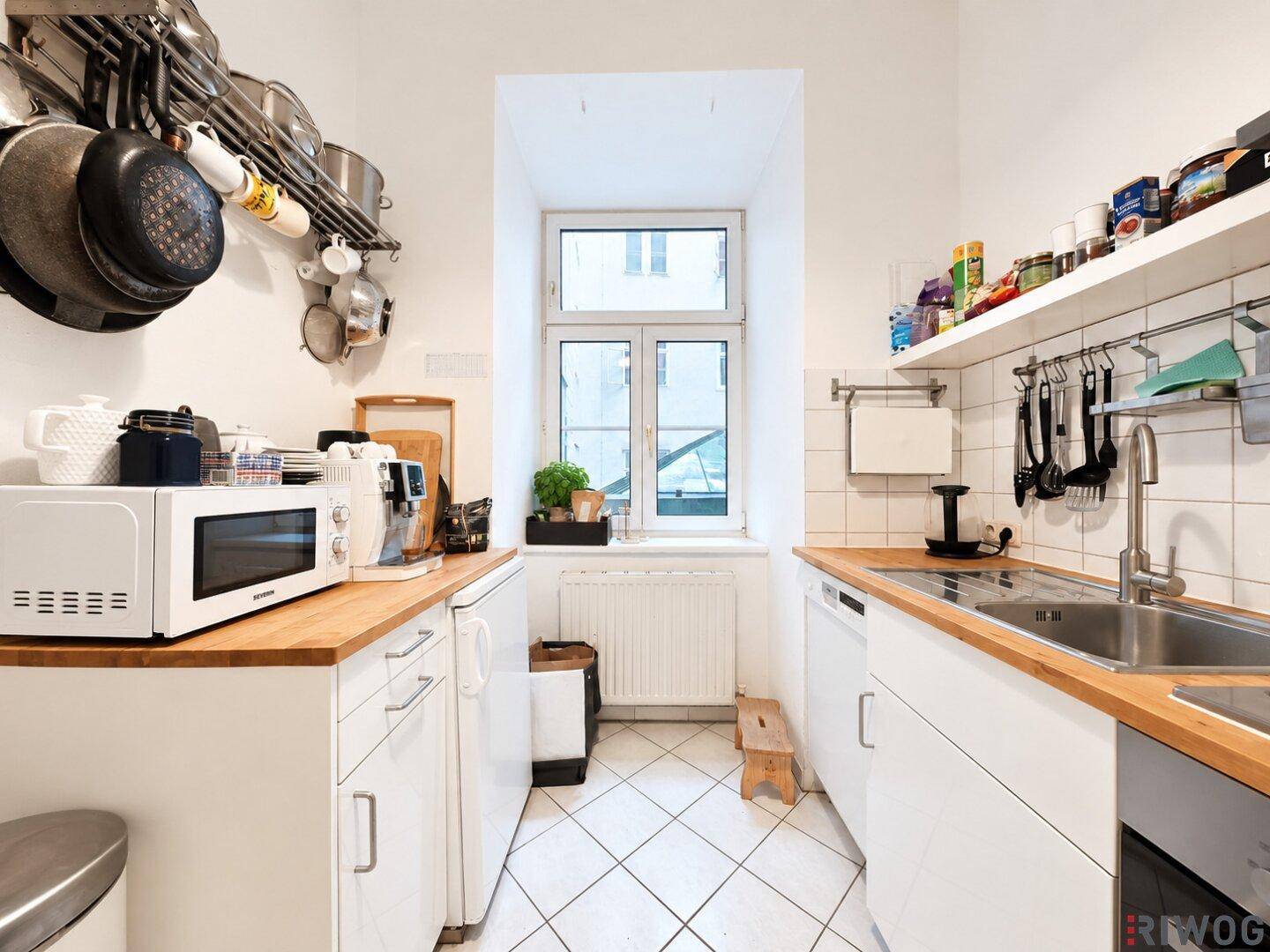 Kleine Küche mit weißen Schränken, Holzarbeitsplatten und einem Fenster.