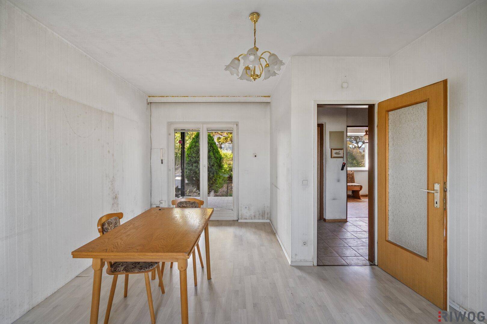 Wohnbereich mit Laminatboden, Esstisch und Zugang zum Garten durch Glastüren.