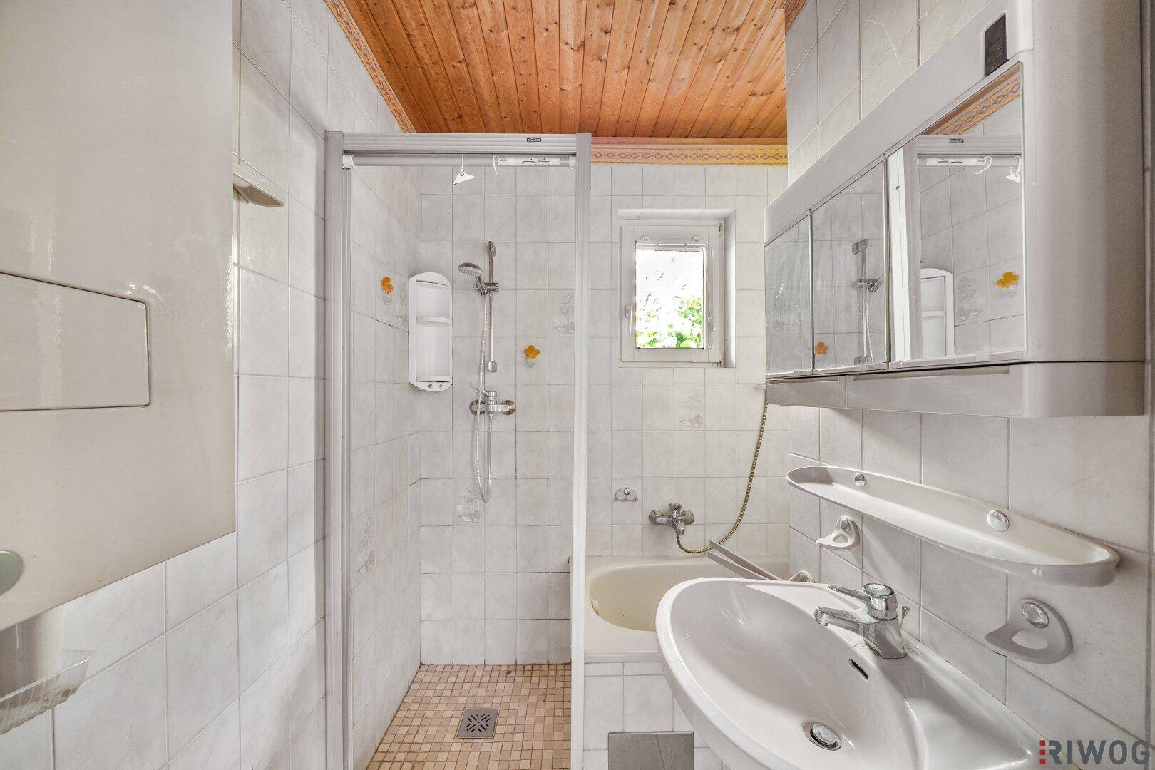 Badezimmer mit Duschkabine, Waschbecken, Spiegelschrank und Fenster.