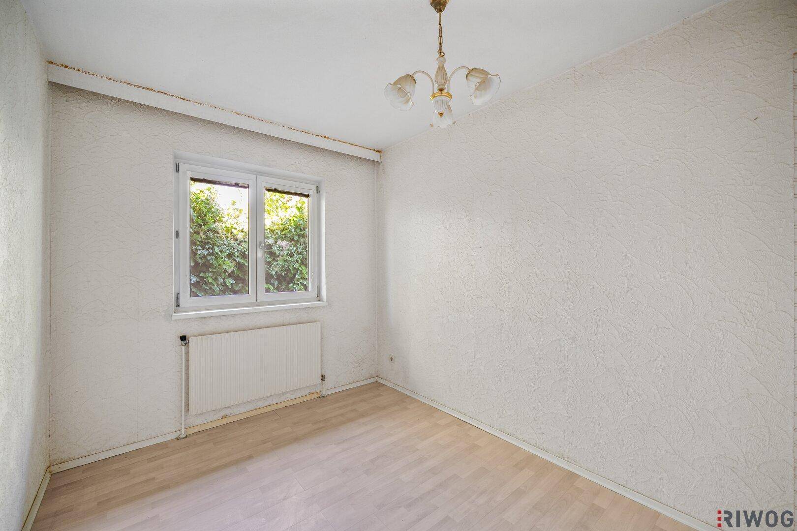 Schlafzimmer mit Laminatboden, Fenster und Heizkörper.