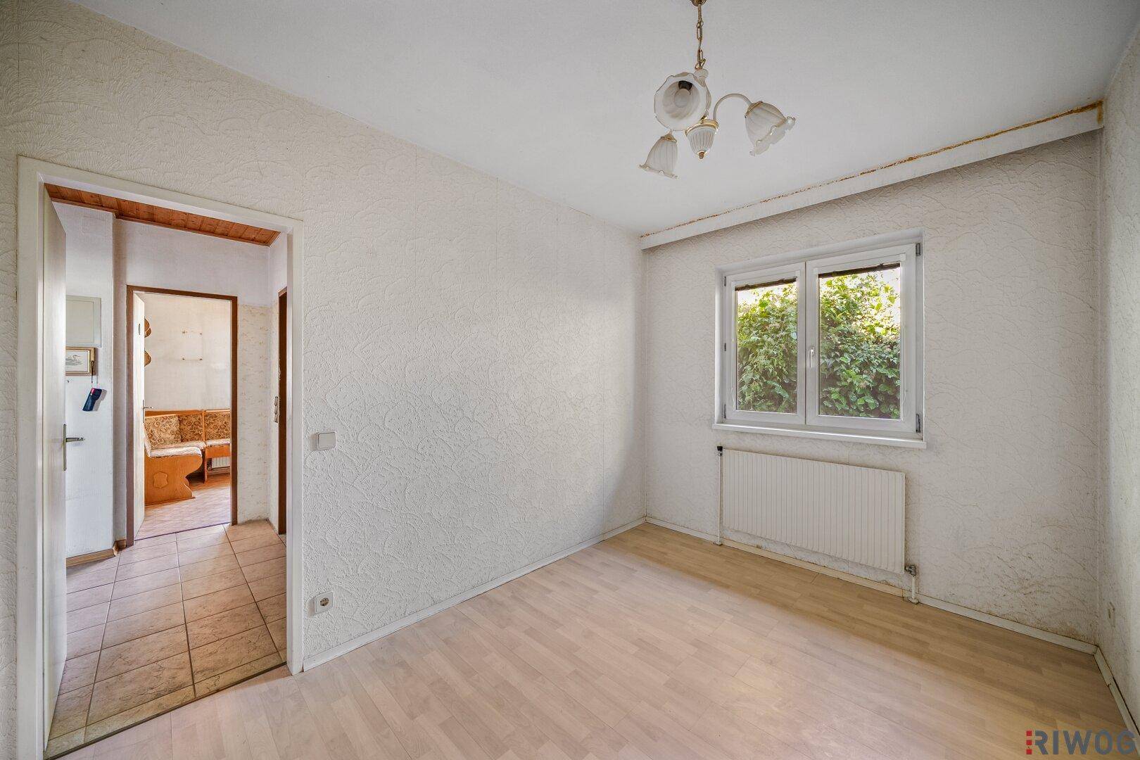 Schlafzimmer mit Laminatboden und offener Tür zu einem angrenzenden Raum.