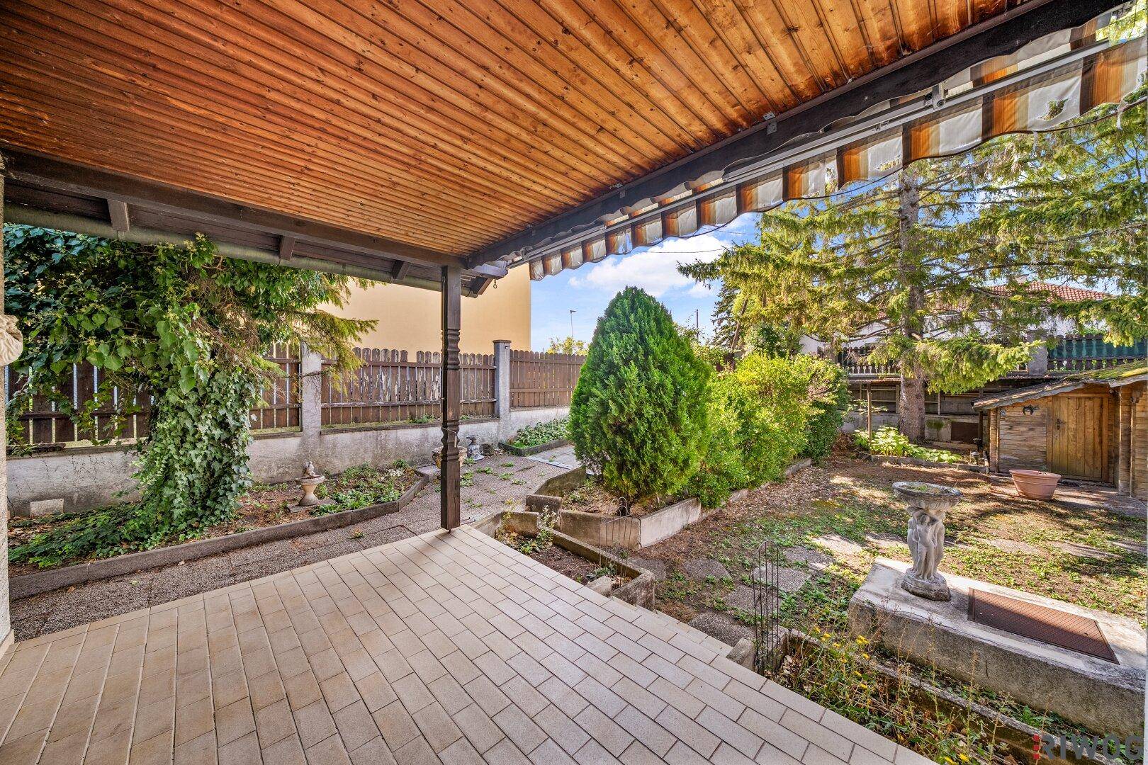 Überdachte Terrasse mit Fliesenboden und Blick in den grünen Gartenbereich.