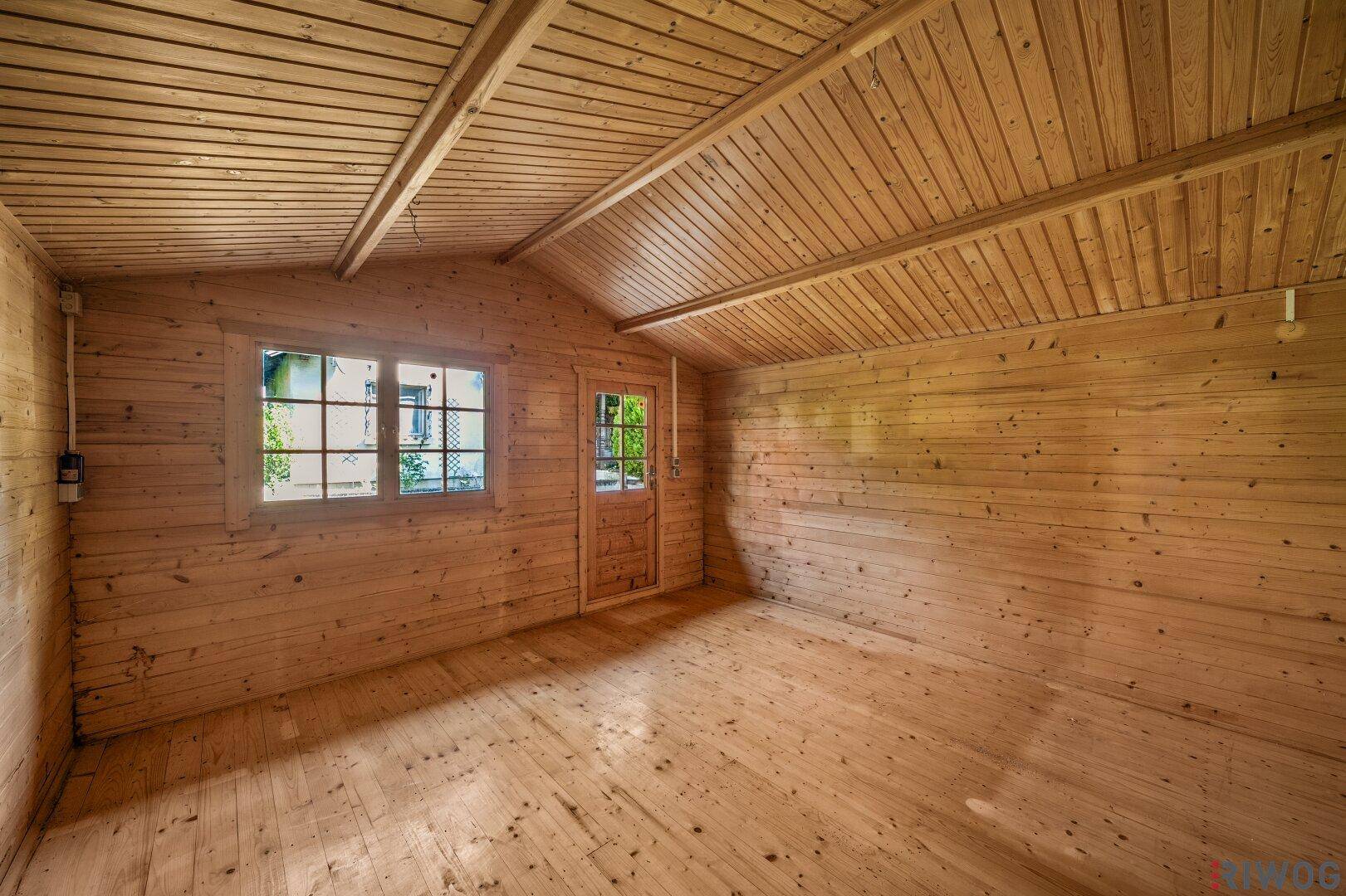 Innenraum des Gartenhauses mit Holzwänden, Holzdecke und Holzboden.