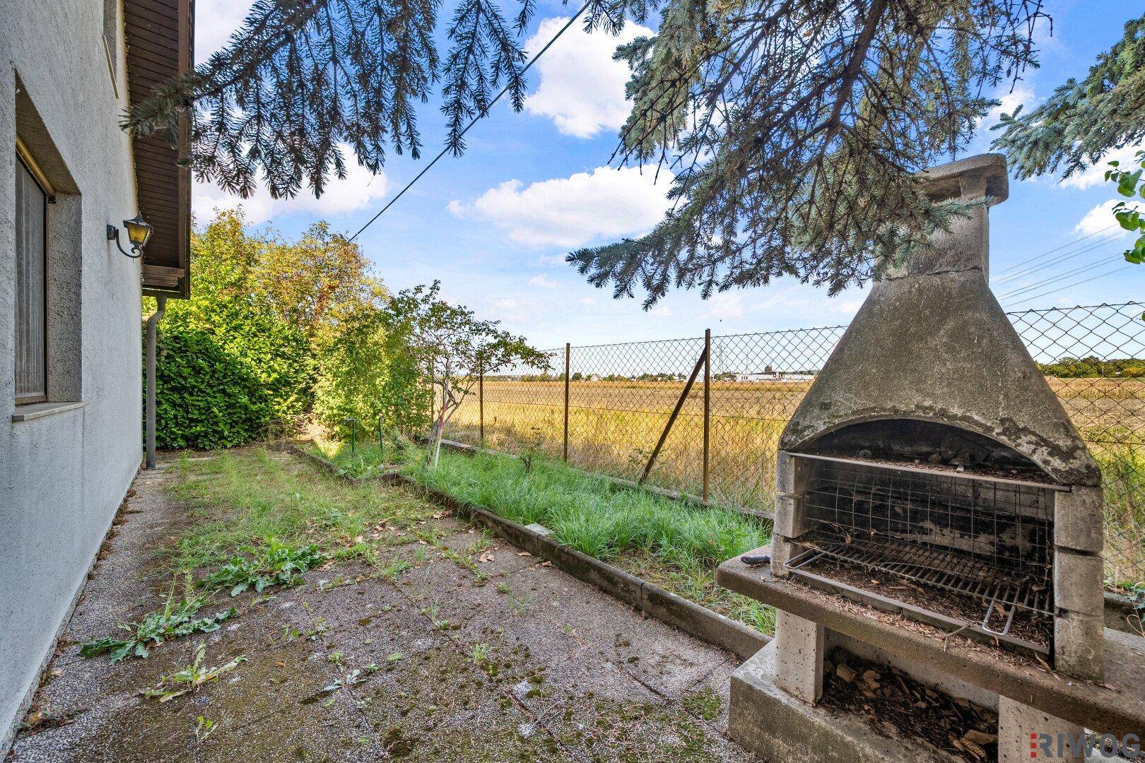 Außenbereich mit gemauertem Grillplatz und weitem Blick auf angrenzende Felder.
