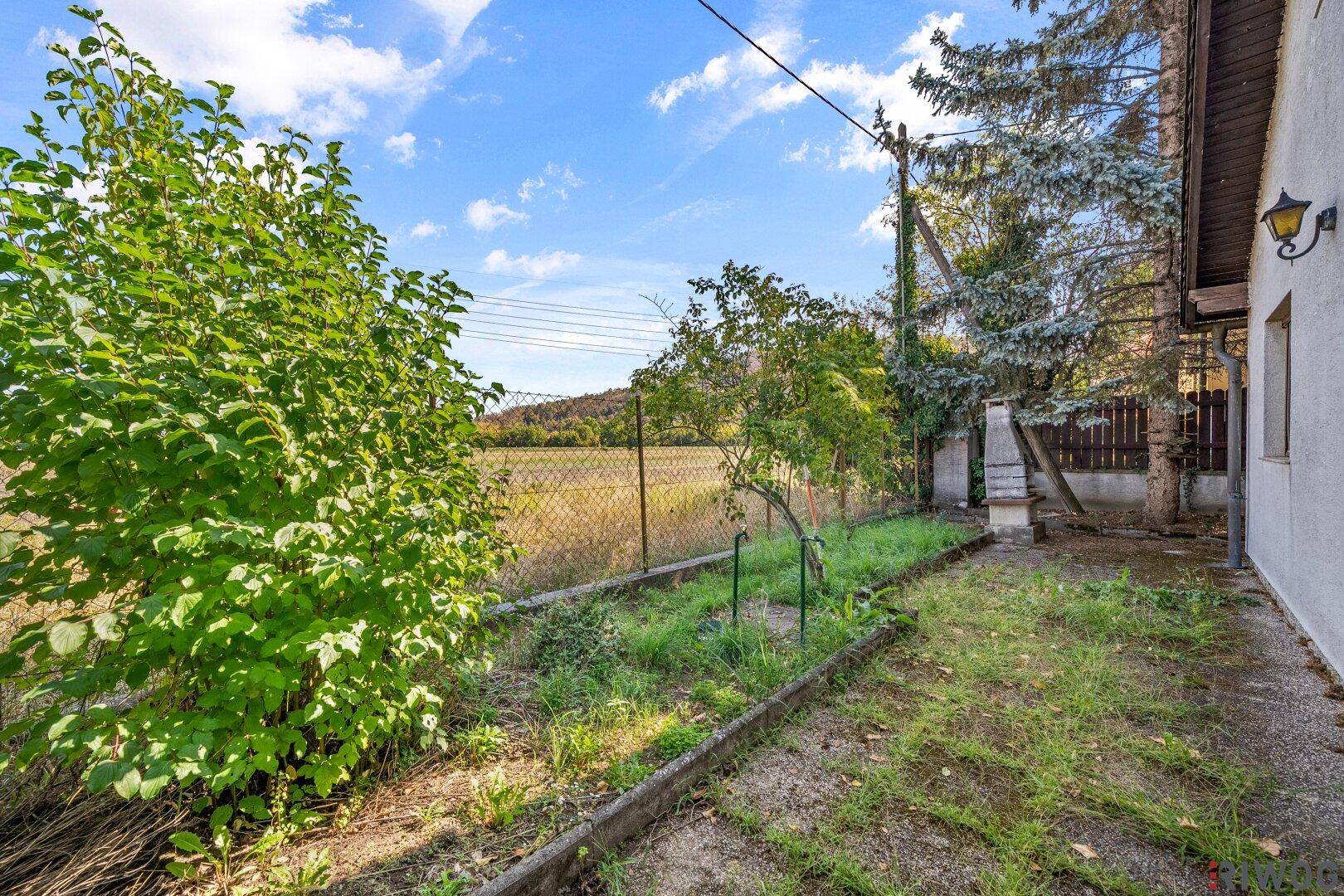 Seitlicher Gartenbereich mit Zaun und freiem Blick auf die umliegende Landschaft.