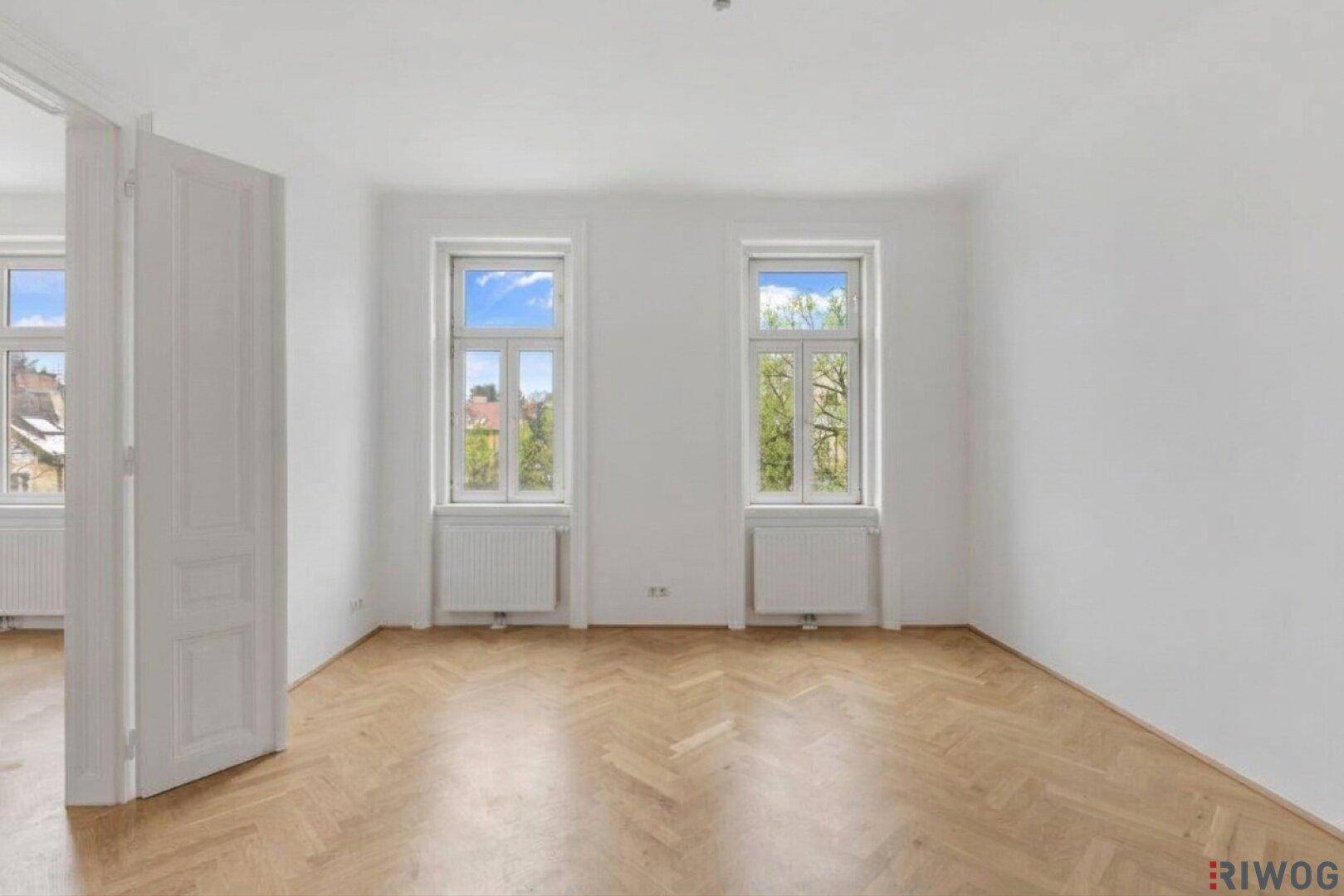 Leeres Schlafzimmer mit hellem Fischgrätparkett, weißen Wänden und zwei Fenstern.