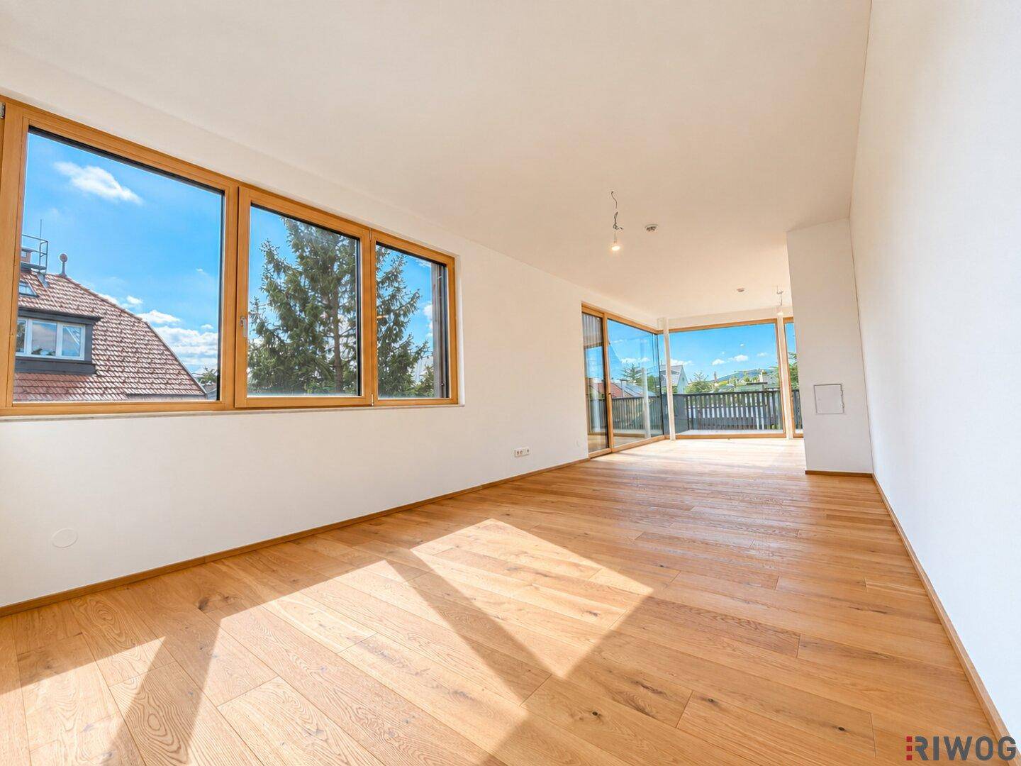 Geräumiger, heller Wohnraum mit Holzboden und großen Fenstern, die einen weiten Blick und Terrassenzugang bieten.