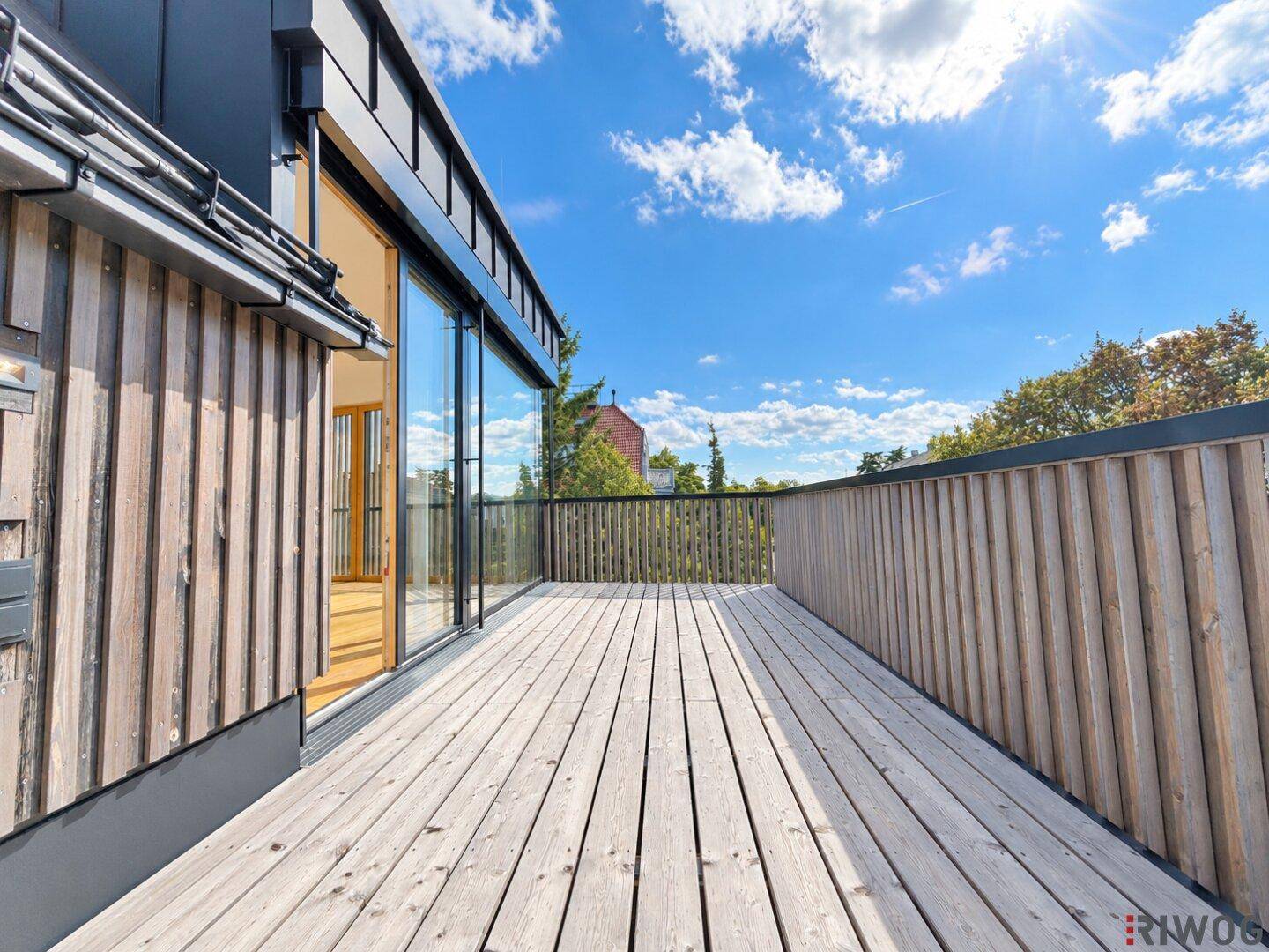 Geräumige Holzterrasse mit Holzwänden und Blick auf die Umgebung unter strahlend blauem Himmel.
