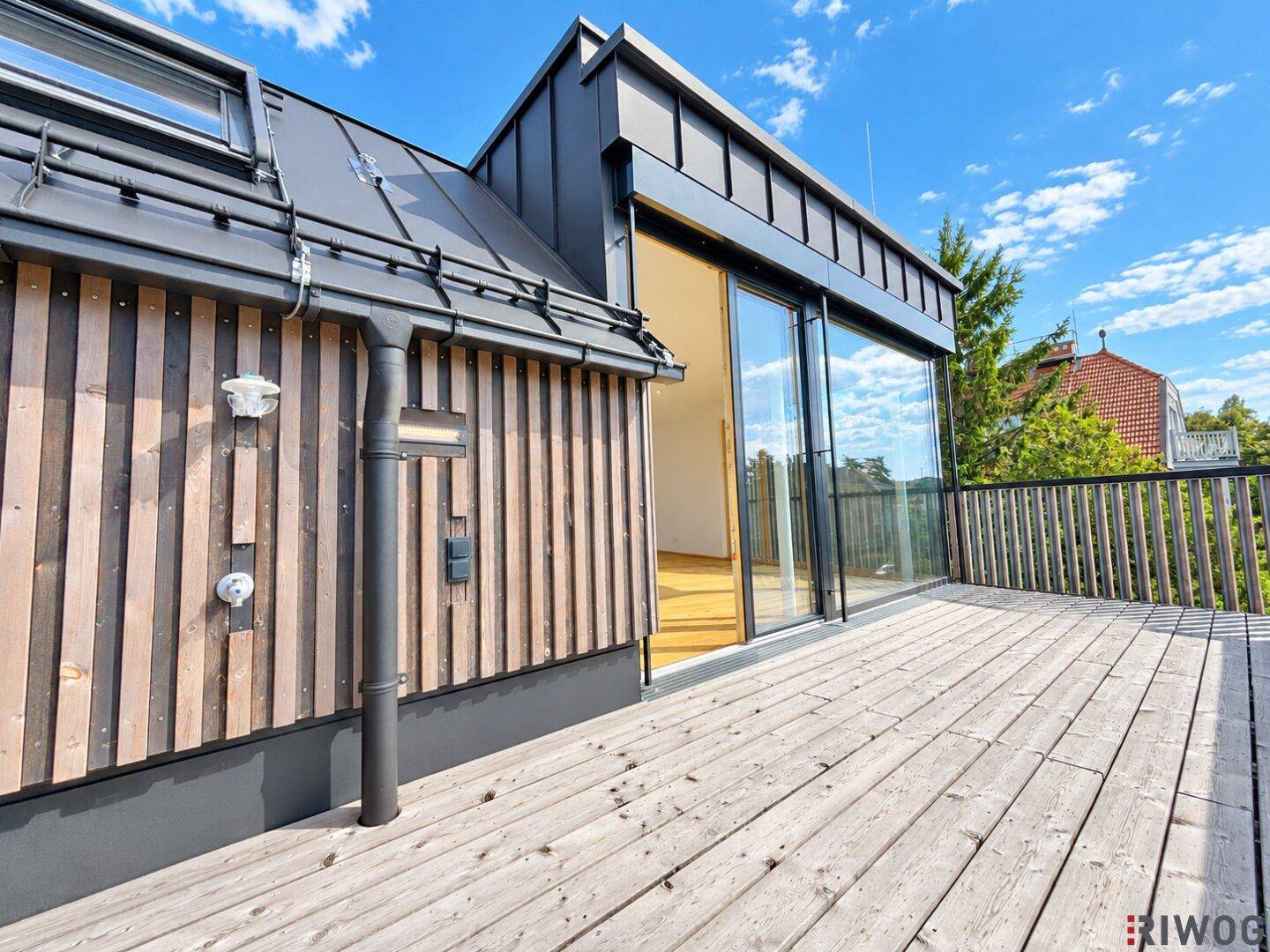 Gebäudeteil mit großer Glasschiebetür, die auf eine weitläufige Holzterrasse führt.