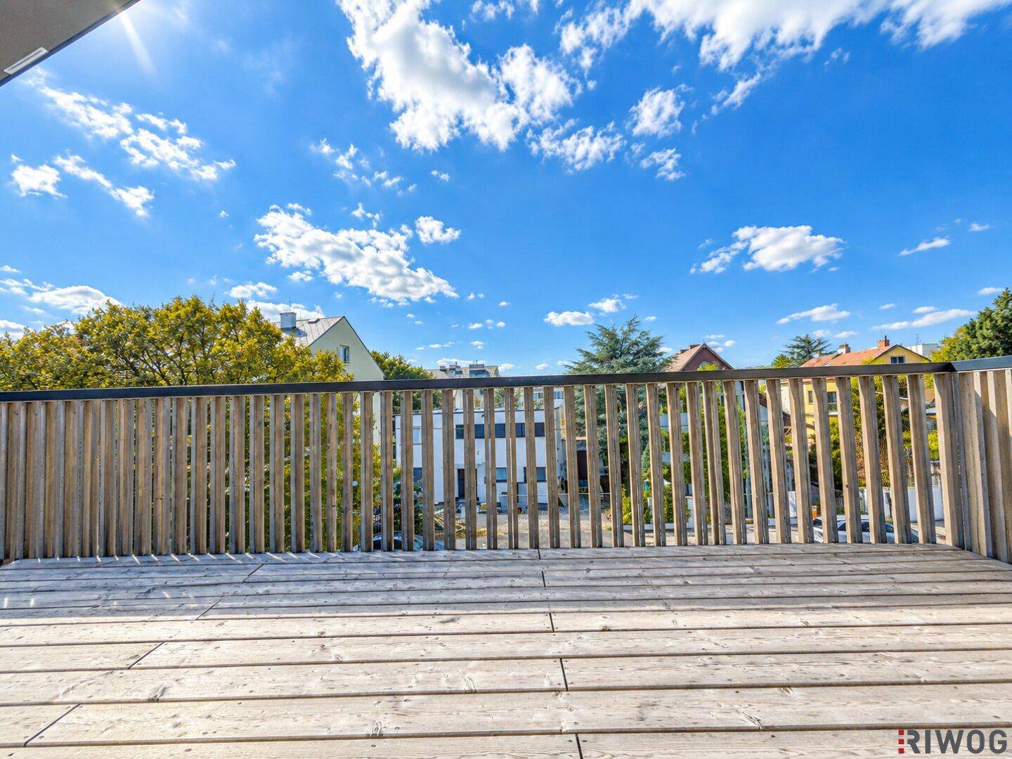 Sonnige Holzterrasse mit vertikalem Holzgeländer, perfekt für Outdoor-Aktivitäten und Entspannung.