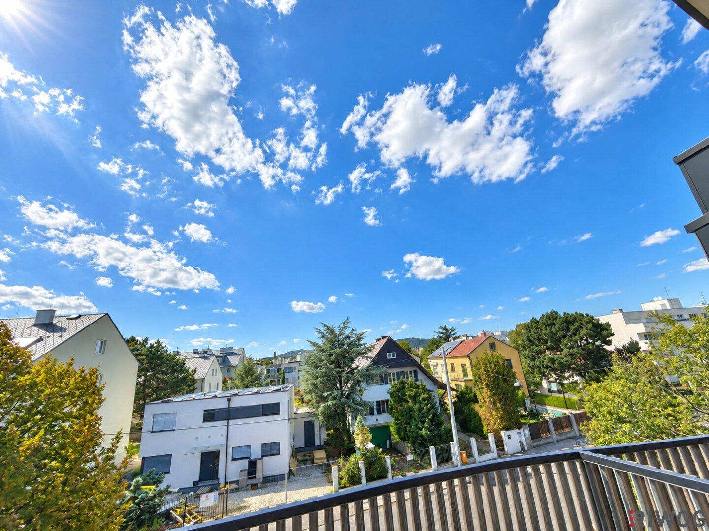 Panoramablick von der Terrasse auf eine ruhige Wohnsiedlung mit viel Grün und blauen Himmel.