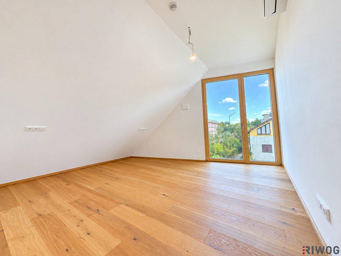 Helles Schlafzimmer mit Holzboden, Dachschräge und großem Fenster mit Blick ins Grüne.