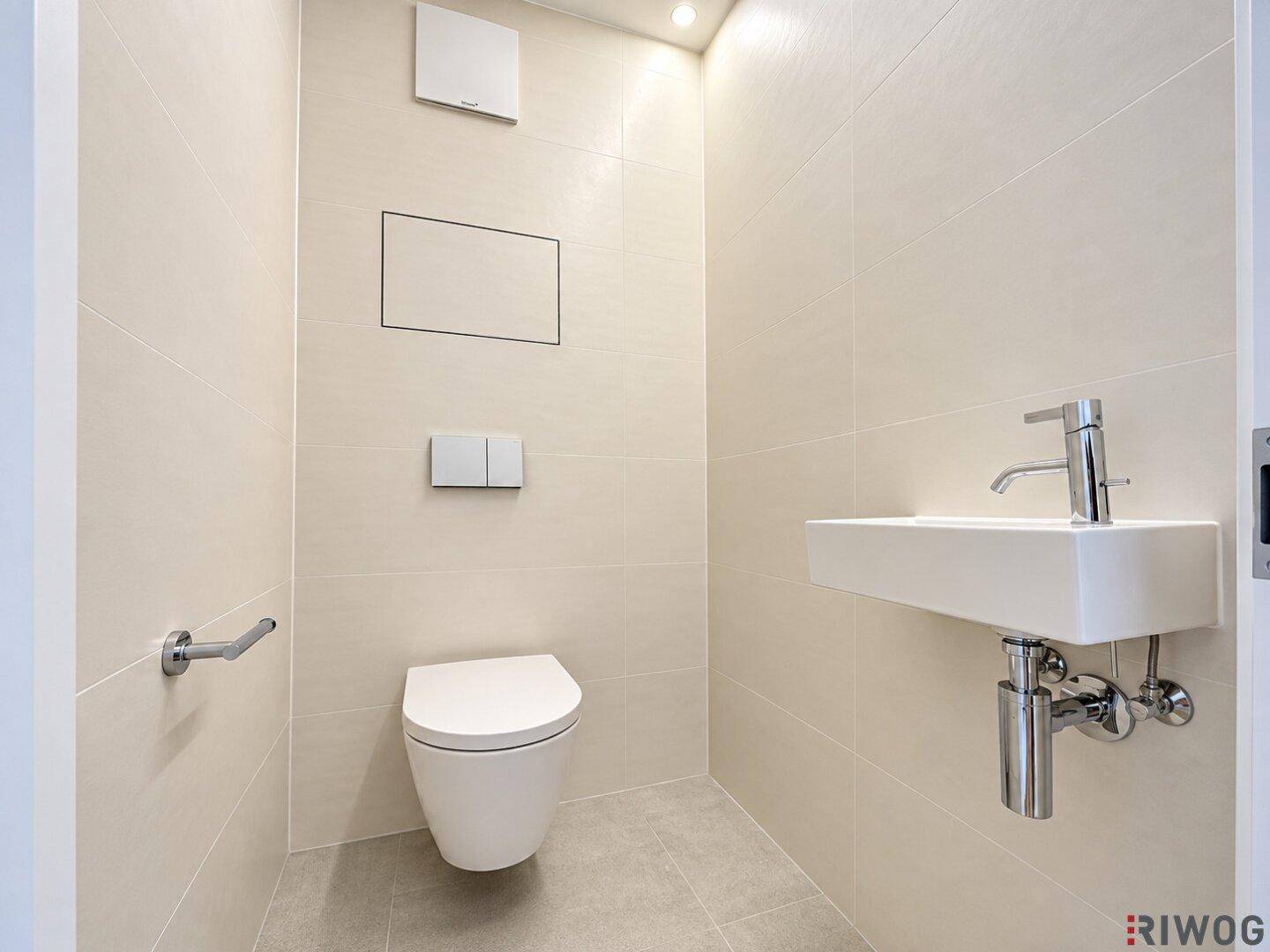 Modernes Gäste-WC mit wandhängender Toilette, kleinem Waschbecken und hellen Fliesen.