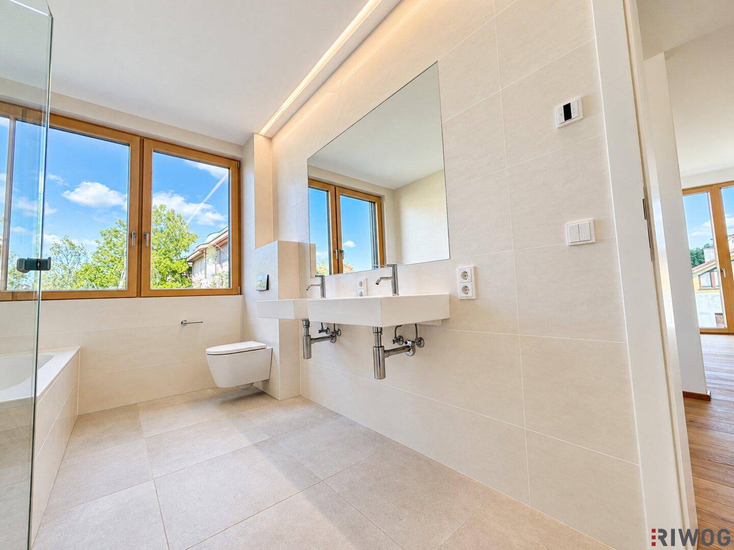 Modernes Badezimmer mit Doppelwaschbecken, Badewanne und großem Fenster für viel Tageslicht.