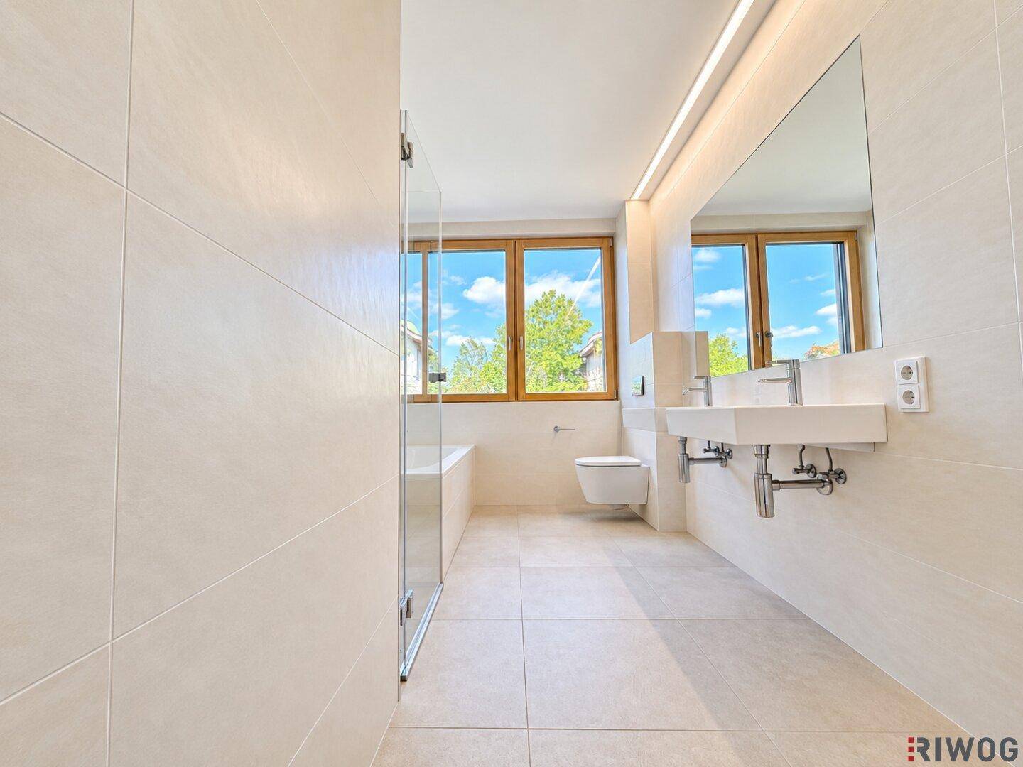 Geräumiges Badezimmer mit Badewanne, Doppelwaschbecken und großen Fenstern, die den Raum erhellen.