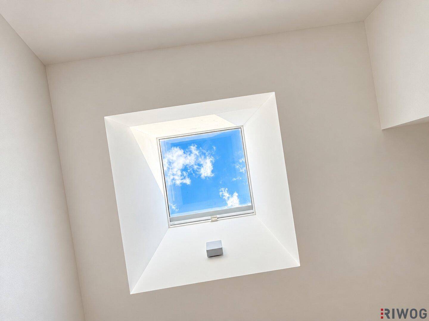 Helles Dachfenster in einer weißen Decke, das den Blick auf den blauen Himmel freigibt.