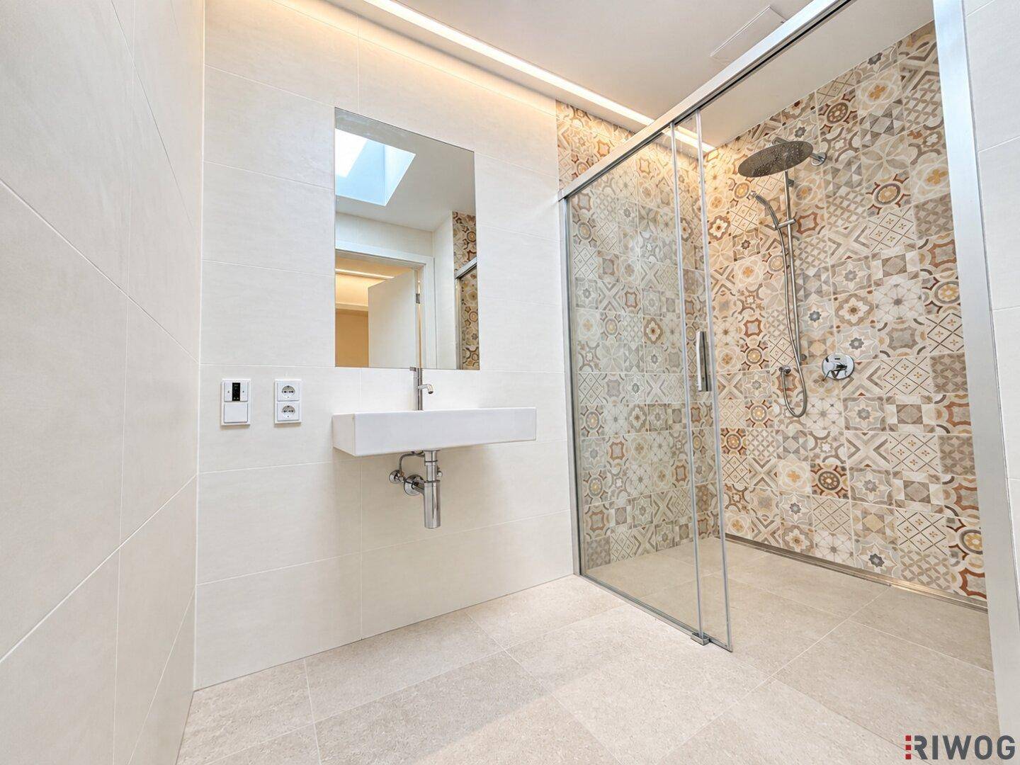 Modernes Badezimmer mit begehbarer Dusche, gemusterten Fliesen und einem Waschbecken unter einem Dachfenster.