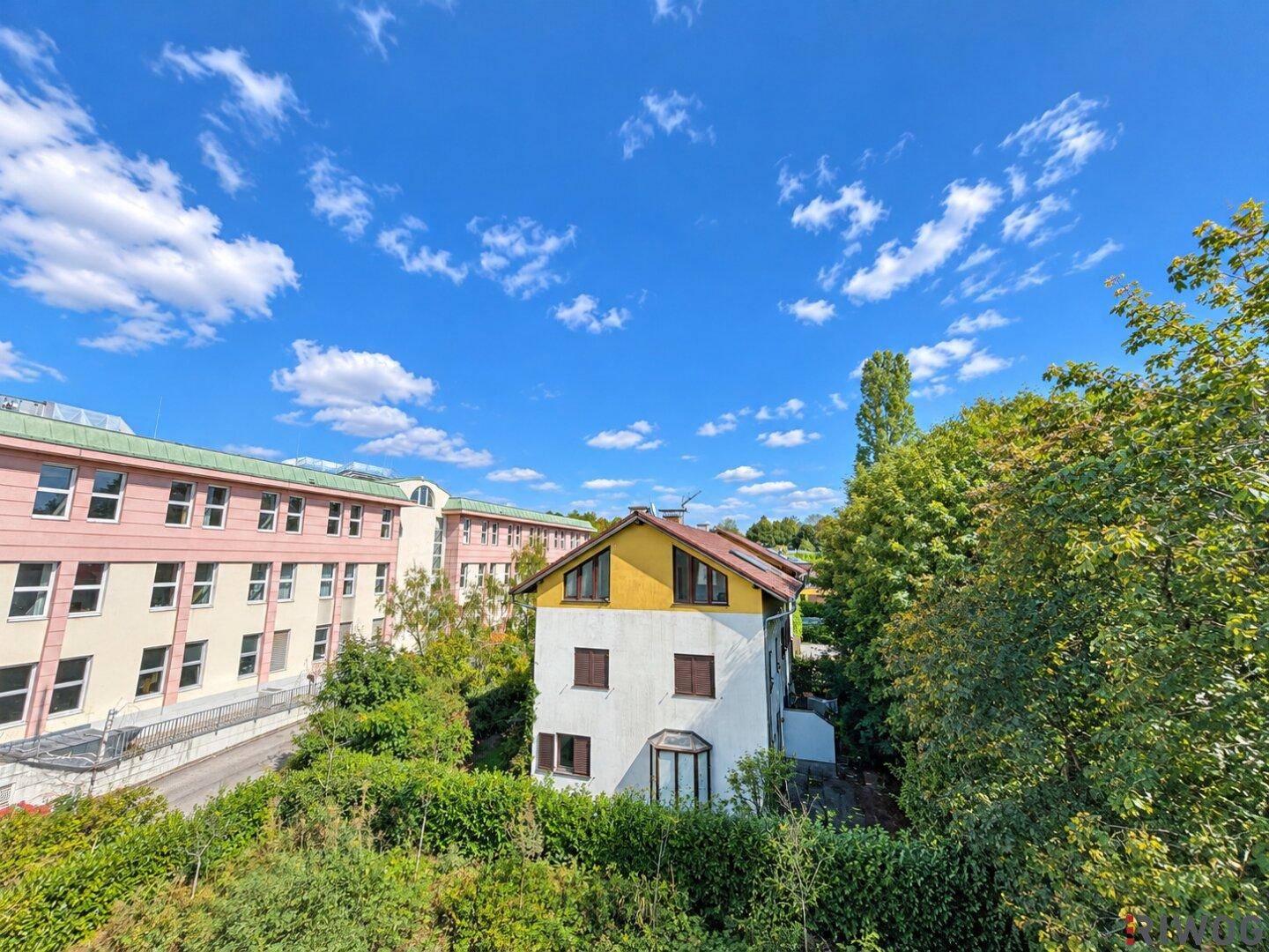 Panoramablick auf die Umgebung mit einem gelben Haus, viel Grün und weiteren Gebäuden unter blauem Himmel.