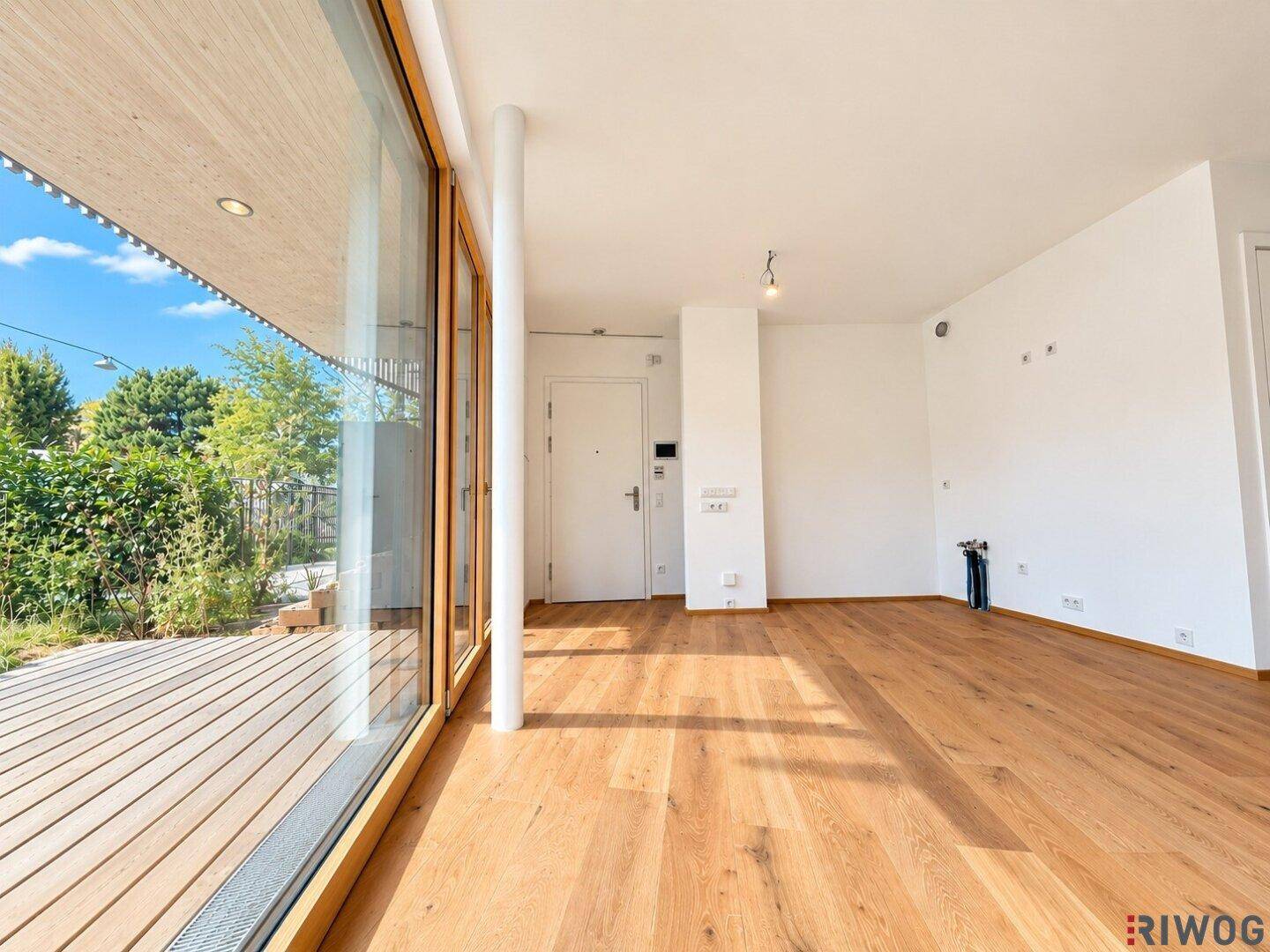 Geräumiger Wohnbereich mit Holzboden und Zugang zur Terrasse durch eine große Glasfront.