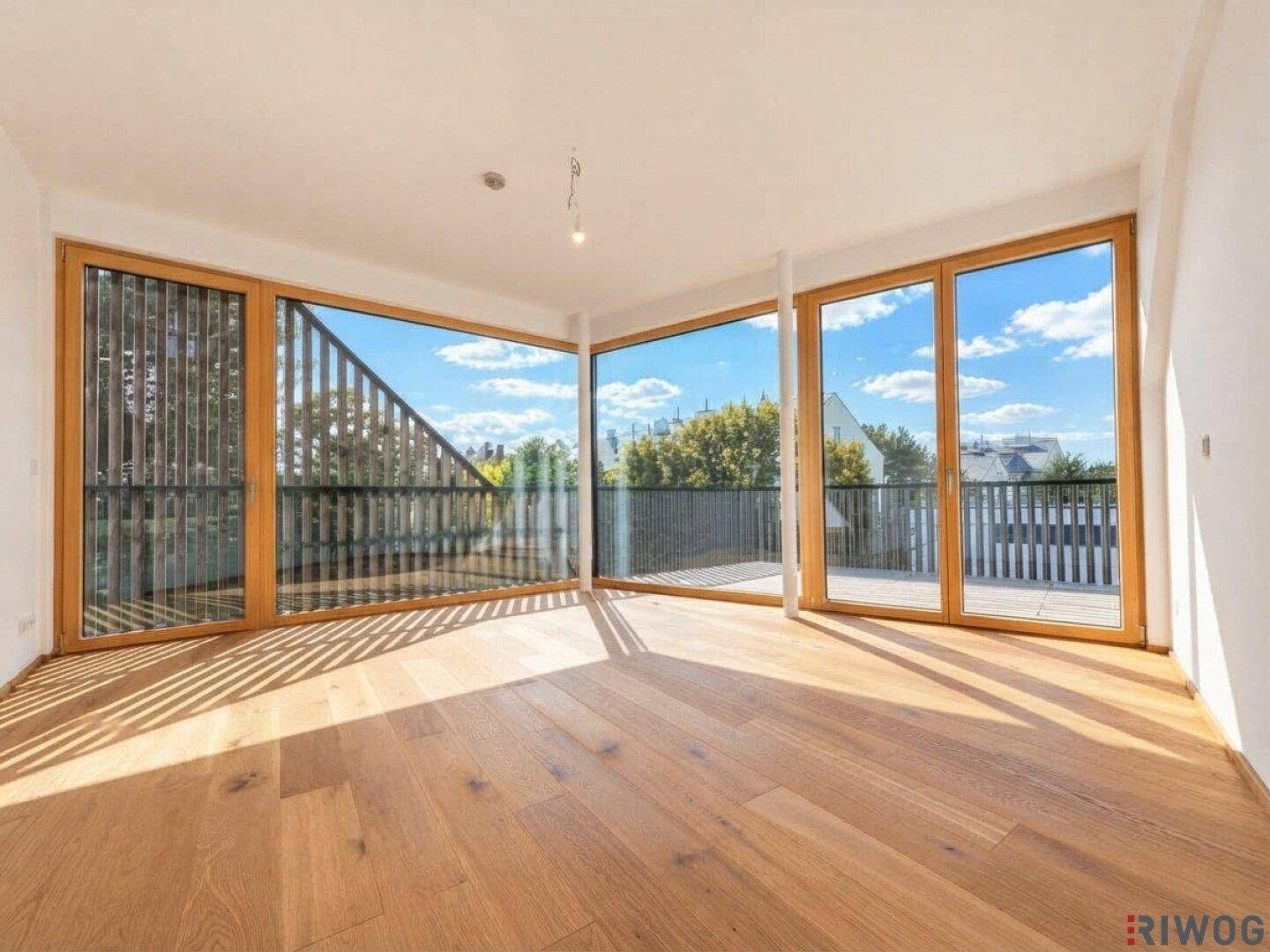 Heller Wohnraum mit großen Fenstern, Holzboden und Zugang zu einer sonnigen Terrasse.