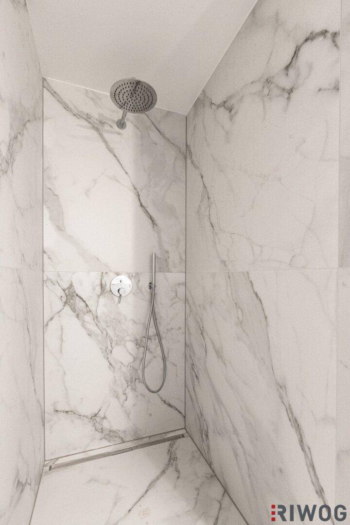 Elegante begehbare Dusche mit Marmorfliesen und einem modernen Regenduschkopf, passend zum luxuriösen Badezimmer.