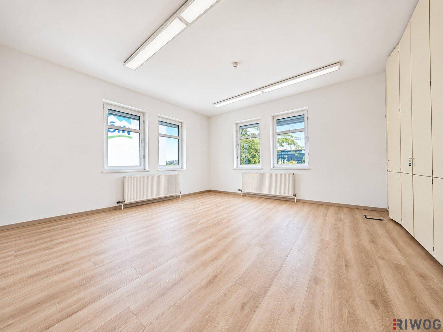 Großes, helles Büro mit mehreren Fenstern, Laminatboden und praktischen Einbauschränken.