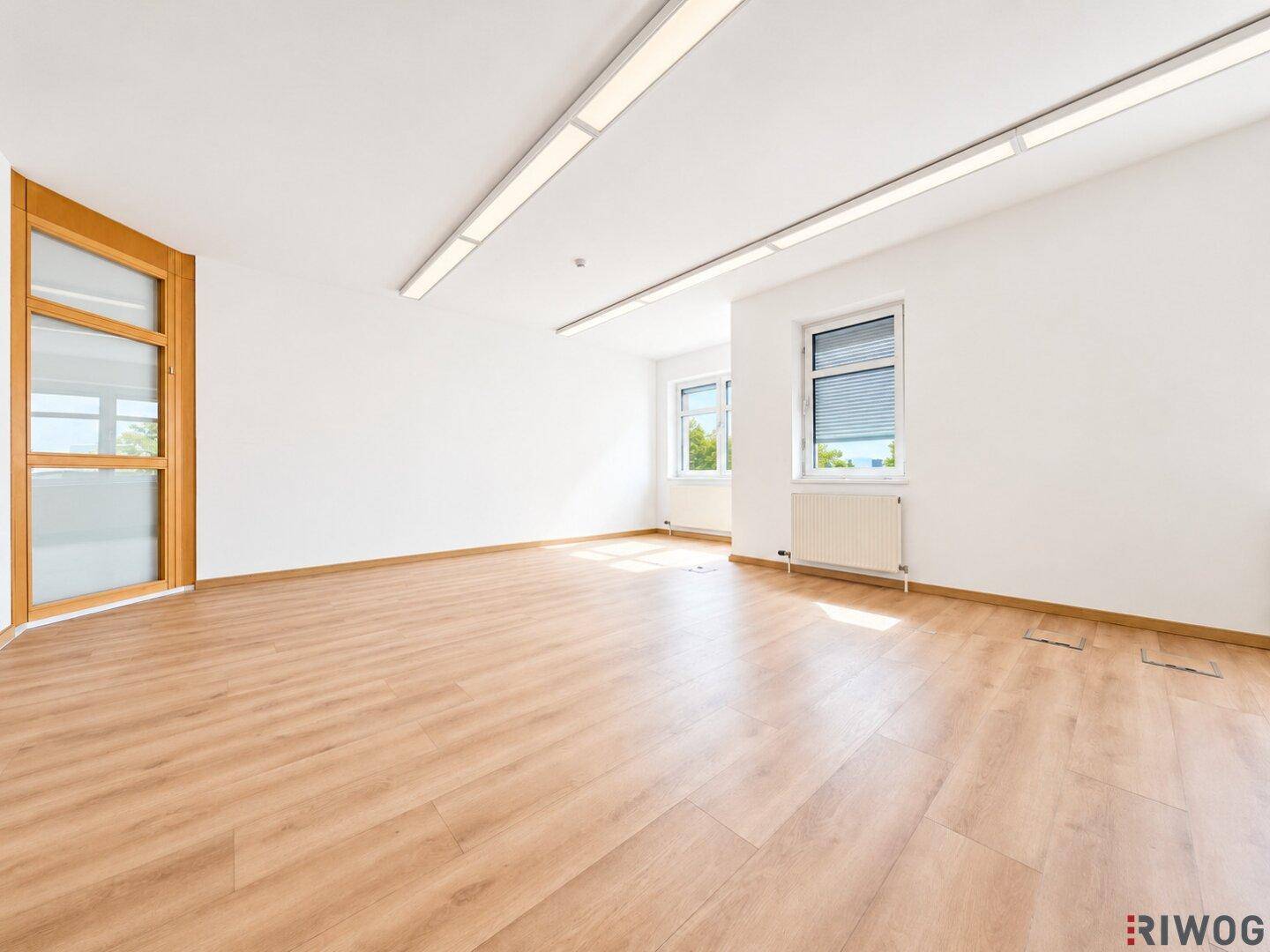 Modernes Büro mit hellem Laminatboden, weißen Wänden und einer stilvollen Holztür mit Glaseinsätzen.