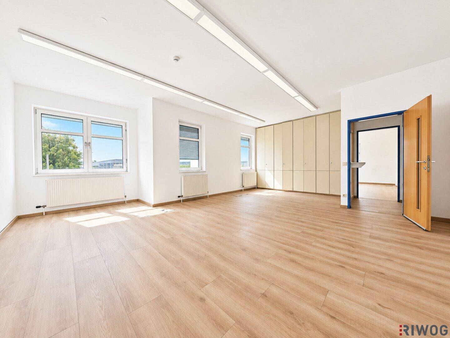 Geräumiges Büro mit Laminatboden, Einbauschränken und einem offenen Durchgang zu einem weiteren Raum.