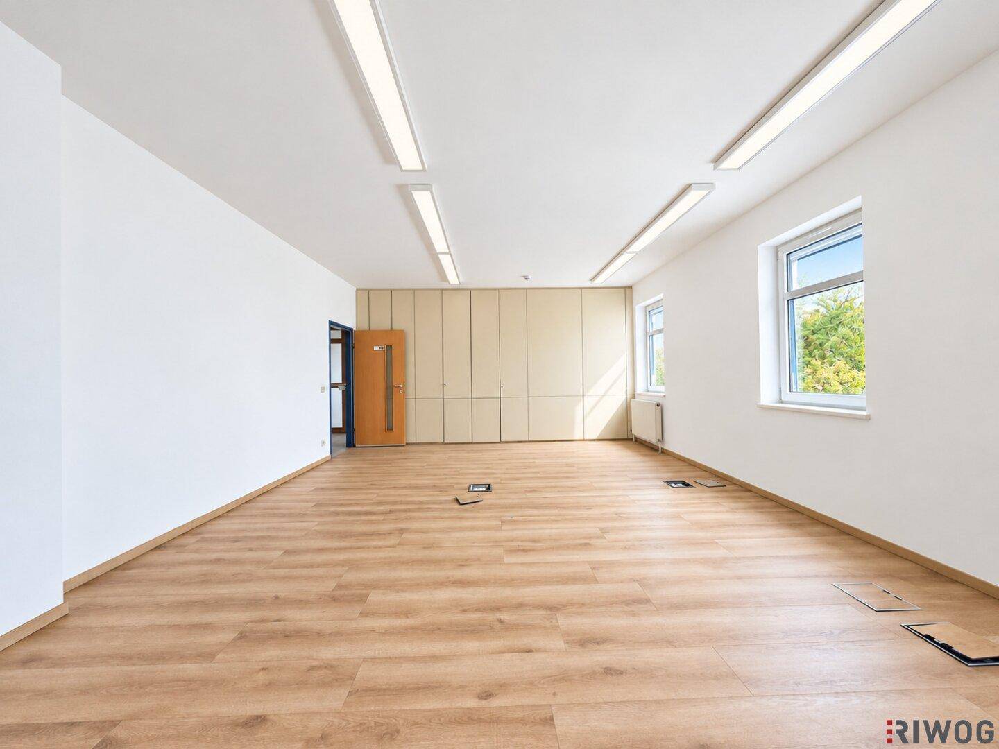 Helles und geräumiges Büro mit Laminatboden, weißen Wänden und integrierten Schränken.