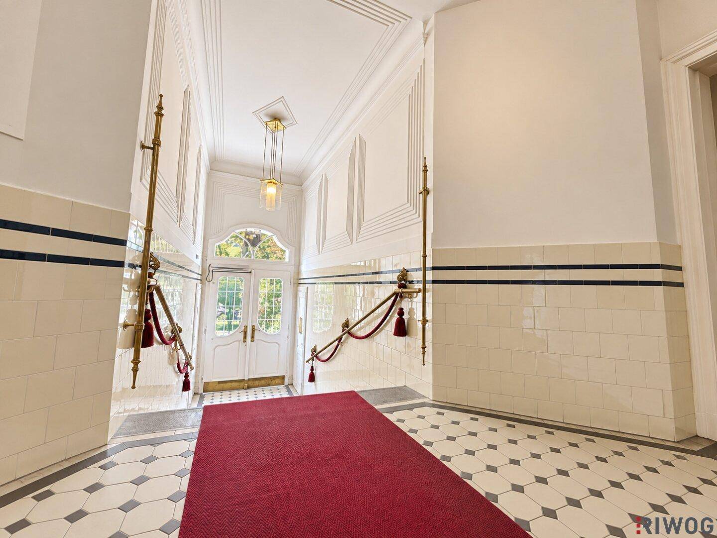 Elegante Eingangshalle mit hohen Decken, dekorativen Wandpaneelen und einem gemusterten Fliesenboden.