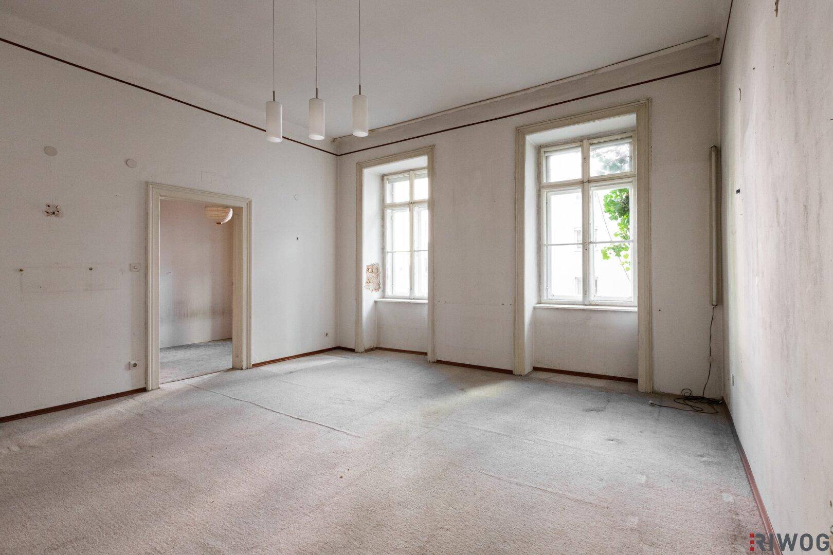 Helles, unmöbliertes Zimmer mit hohen Decken und zwei großen Fenstern, ideal für Renovierung.