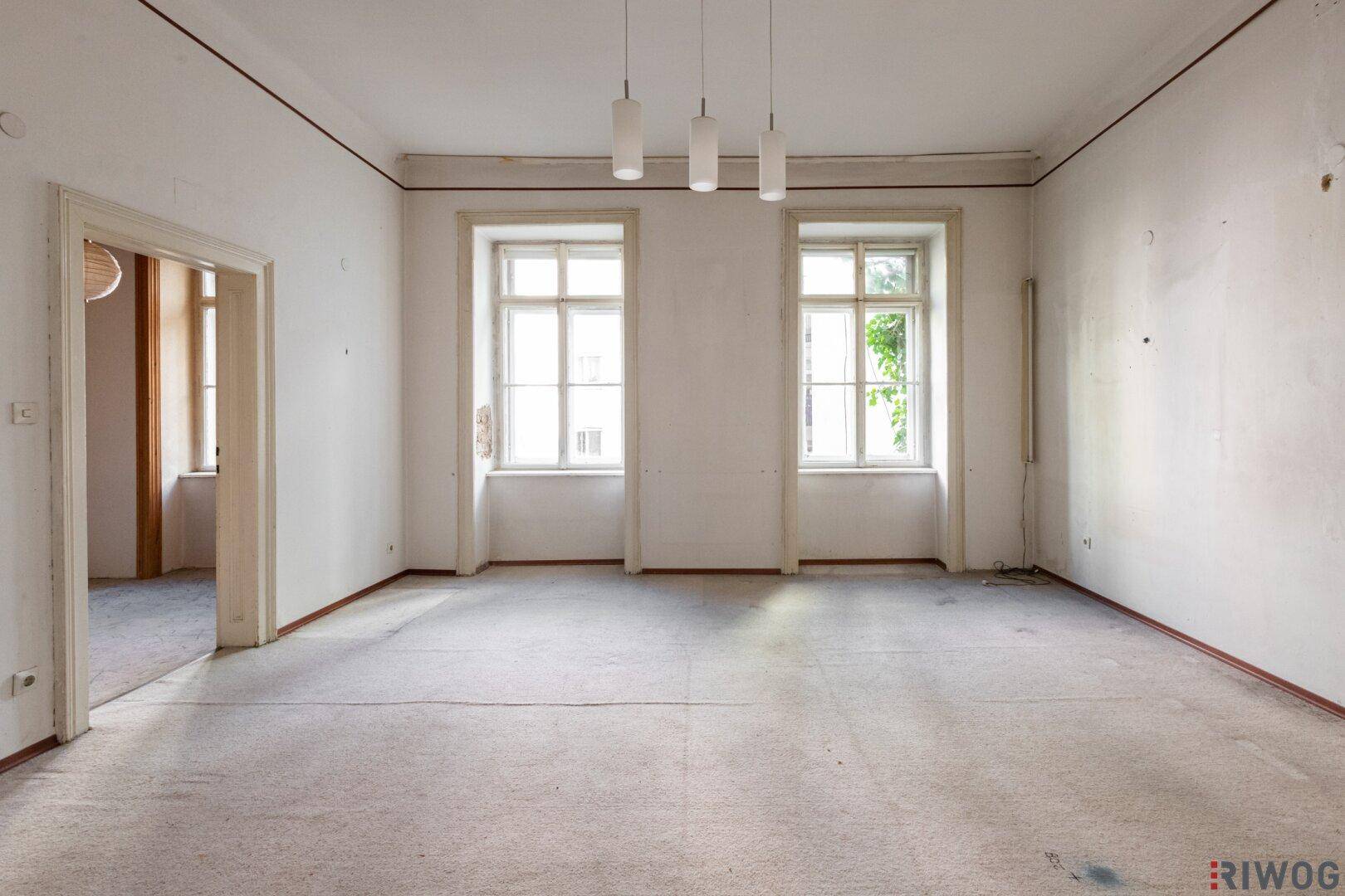Geräumiges, unmöbliertes Zimmer mit zwei großen Fenstern und Teppichboden, bereit zur Renovierung.